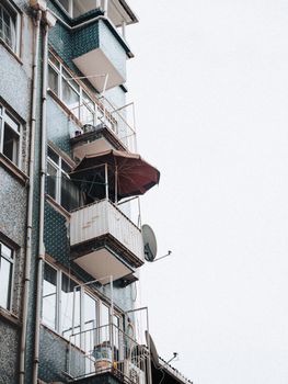 Urban apartment building facade with balconies and an umbrella on a cloudy day.