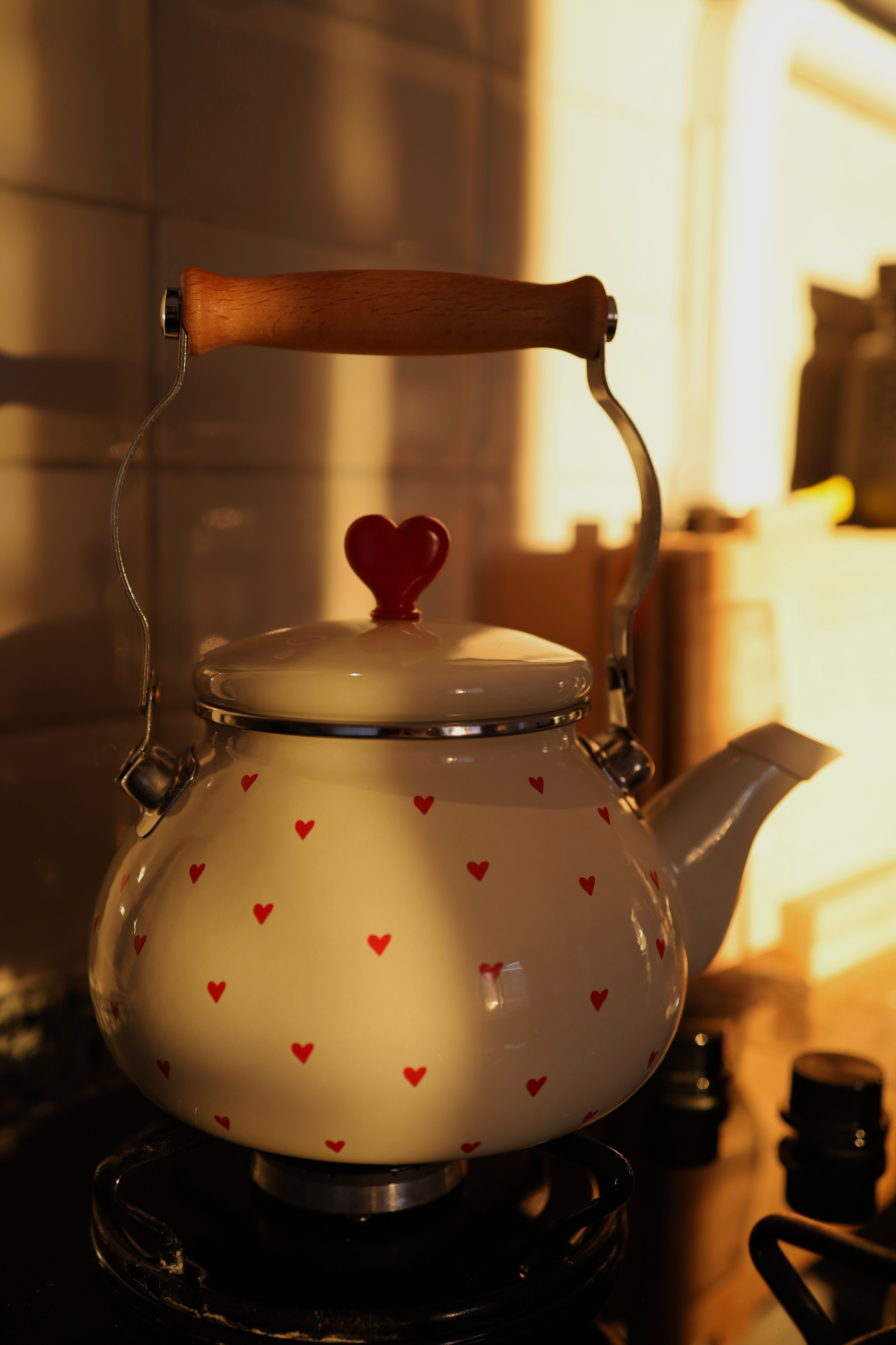 A cozy kitchen scene with a heart-decorated teapot lit by warm sunlight.