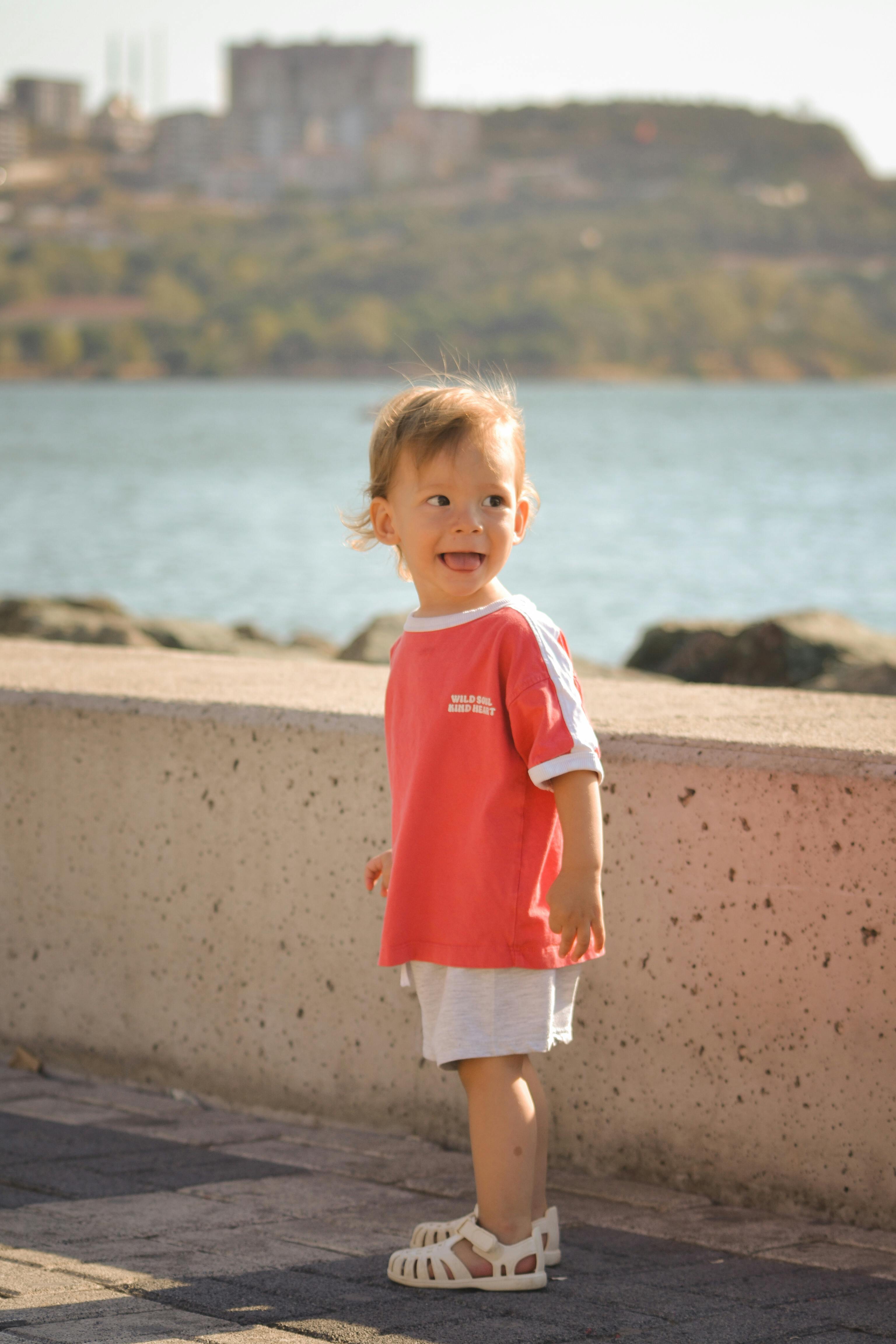 無料 元気な幼児が海沿いの遊歩道に立って、晴れた天気を楽しんでいます。 写真素材