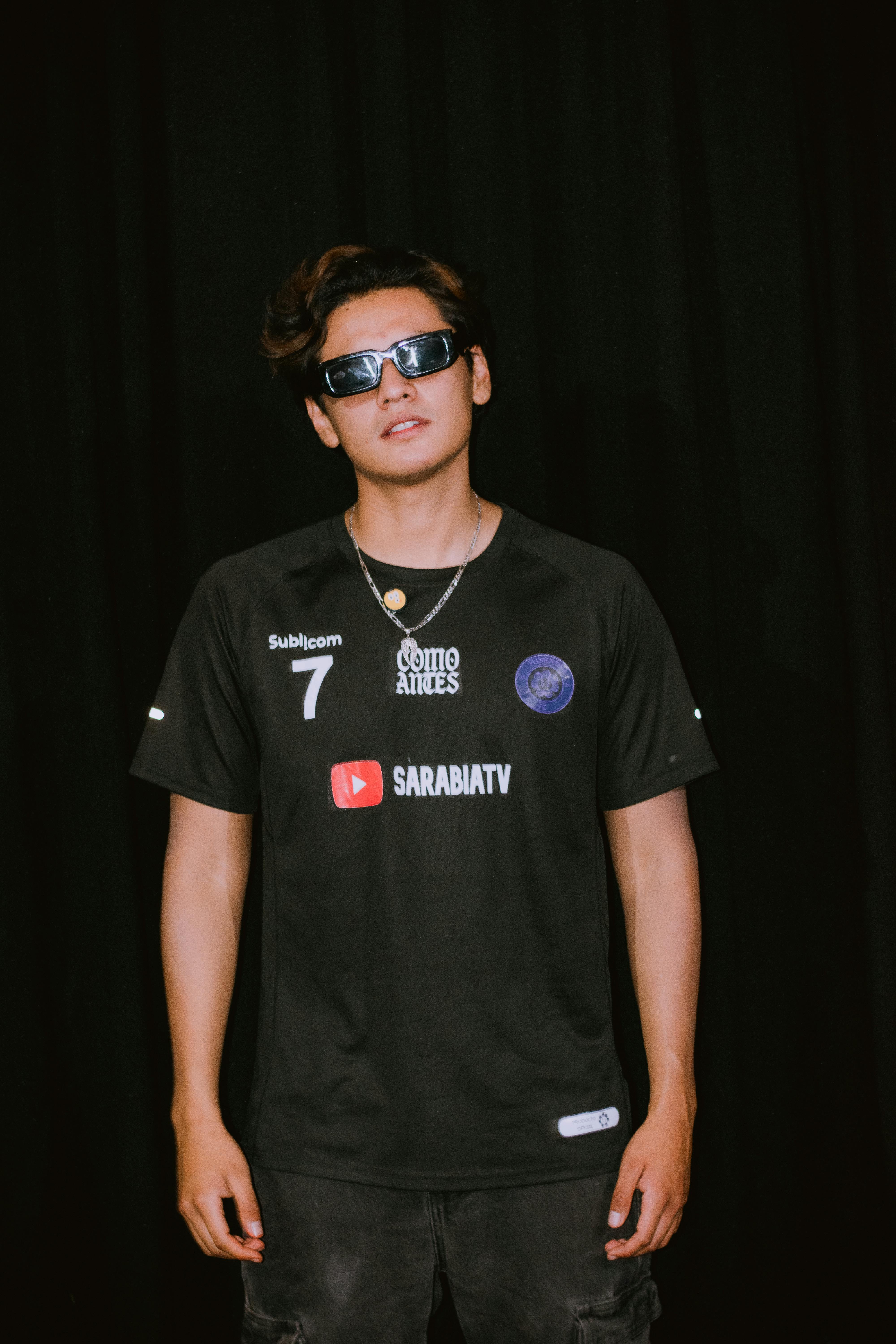 Fashionable young man wearing sunglasses and a black shirt in a relaxed pose.
