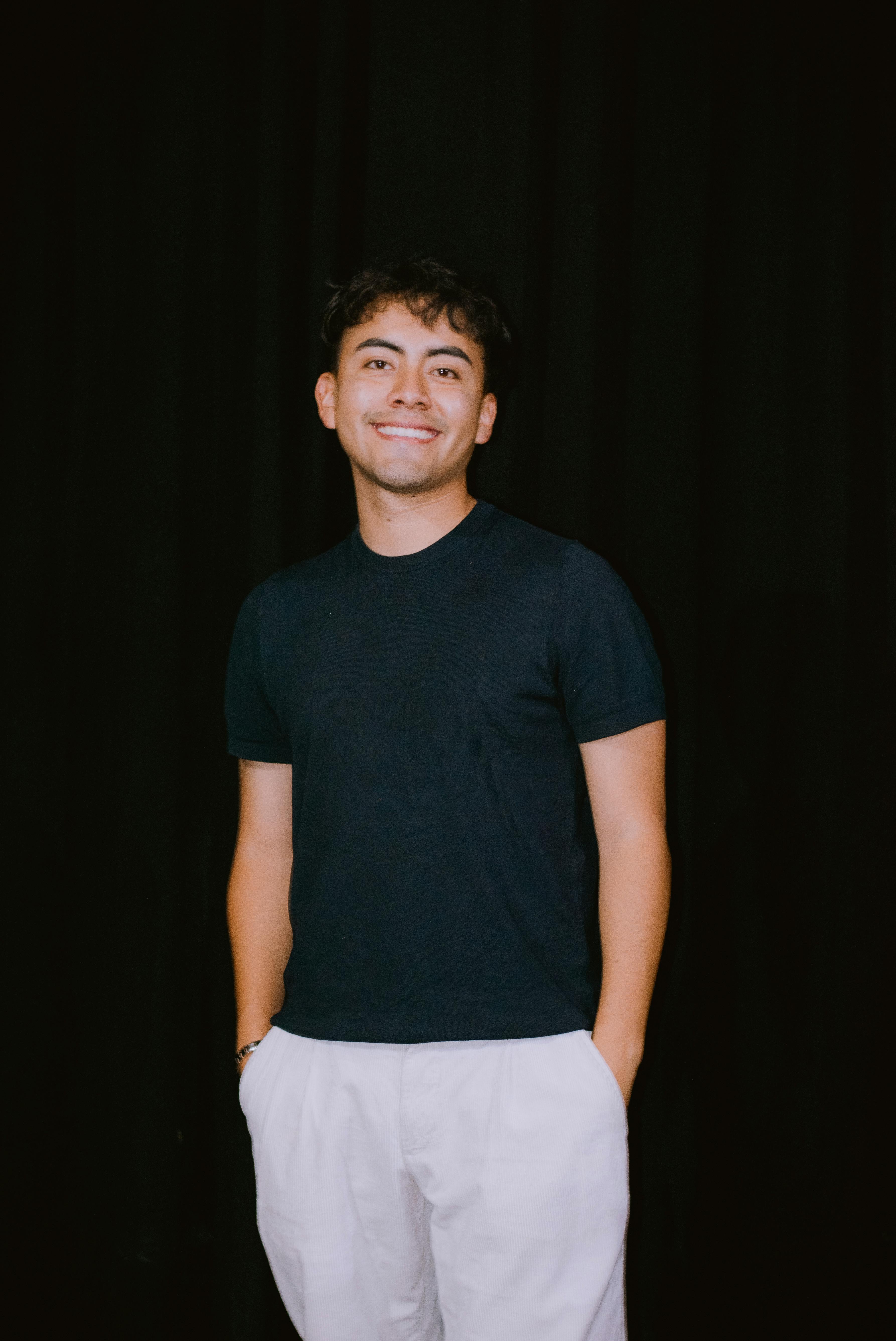 Portrait of a young adult in casual attire against a black background, exuding confidence.