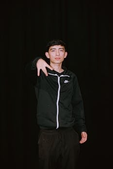 Portrait of a young man in a black tracksuit posing with confidence against a dark background