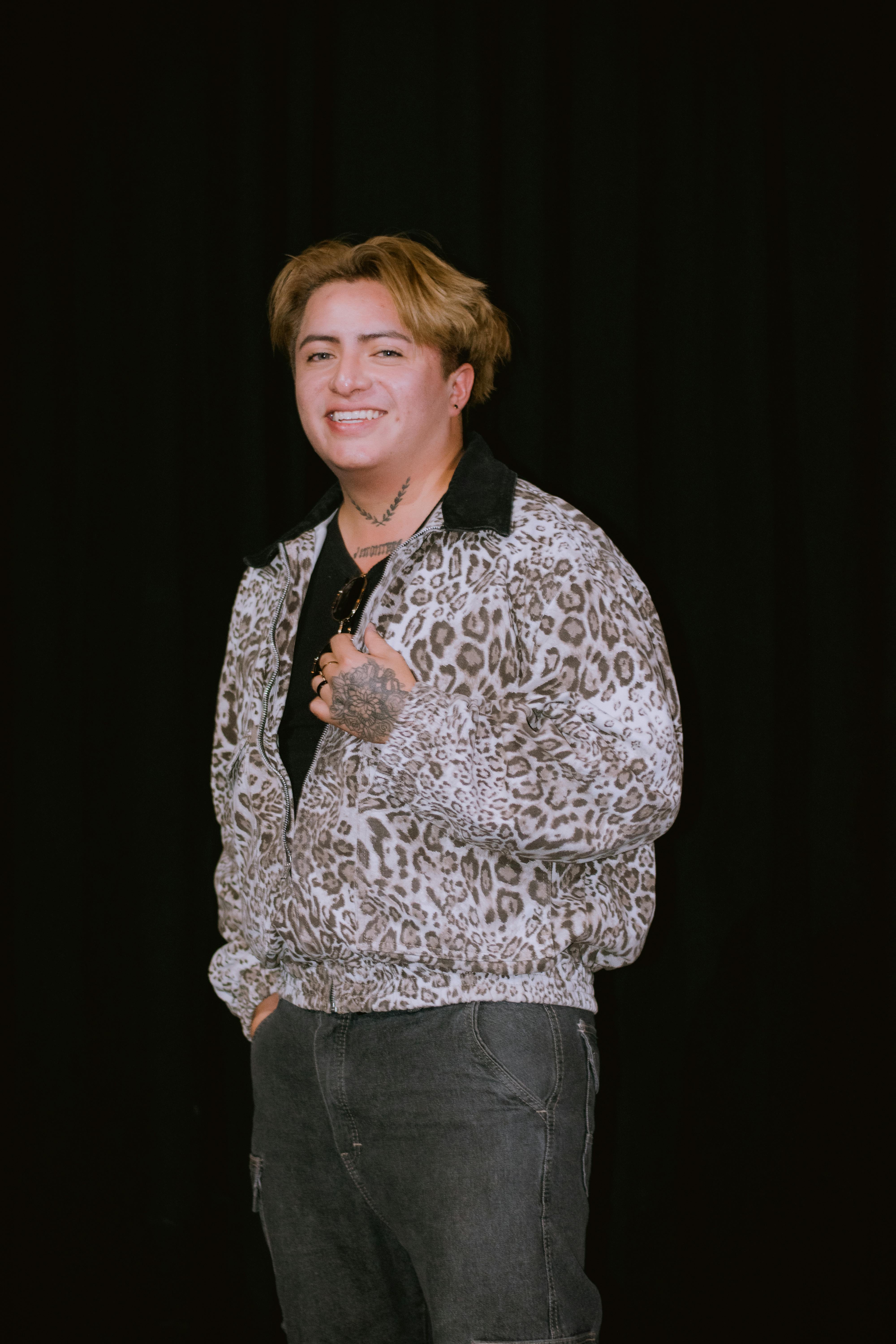 無料 ヒョウ柄のジャケットを着て、暗い背景に対してポーズをとる笑顔の若者。 写真素材