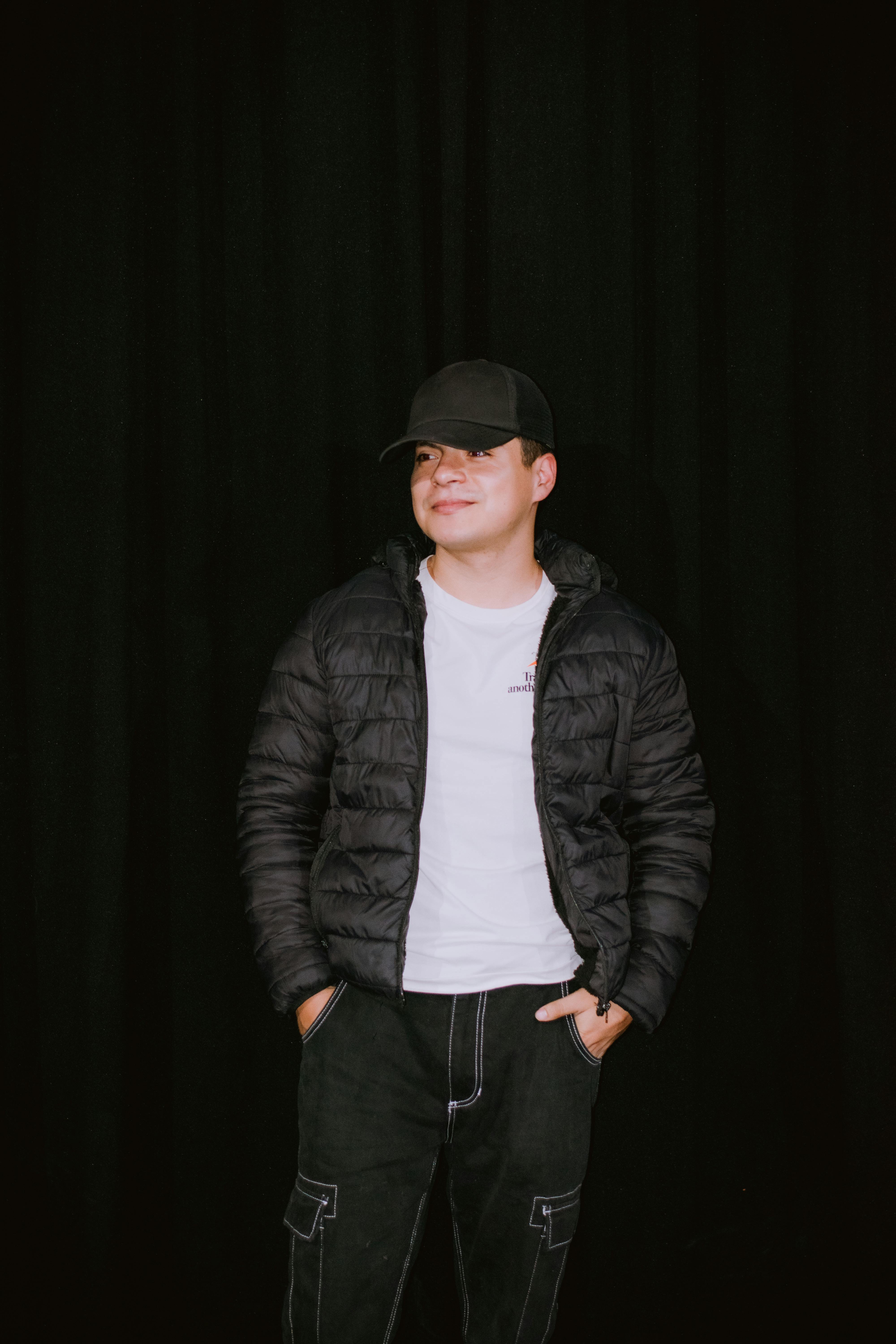 Free A stylish young man wearing a casual black jacket, cap, and white shirt against a dark background. Stock Photo