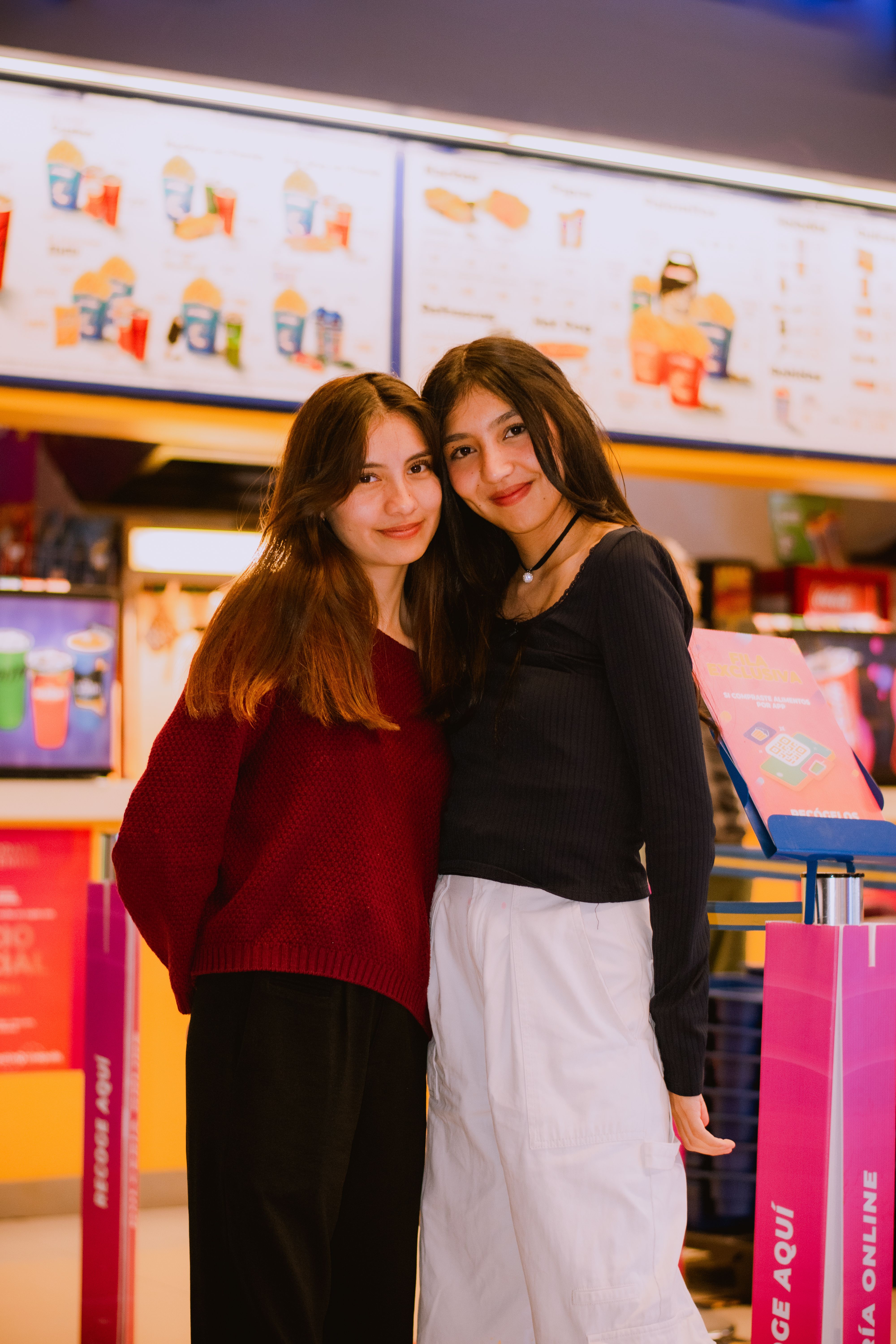 Two young women smiling together indoors at a shopping center in Puebla, Mexico.