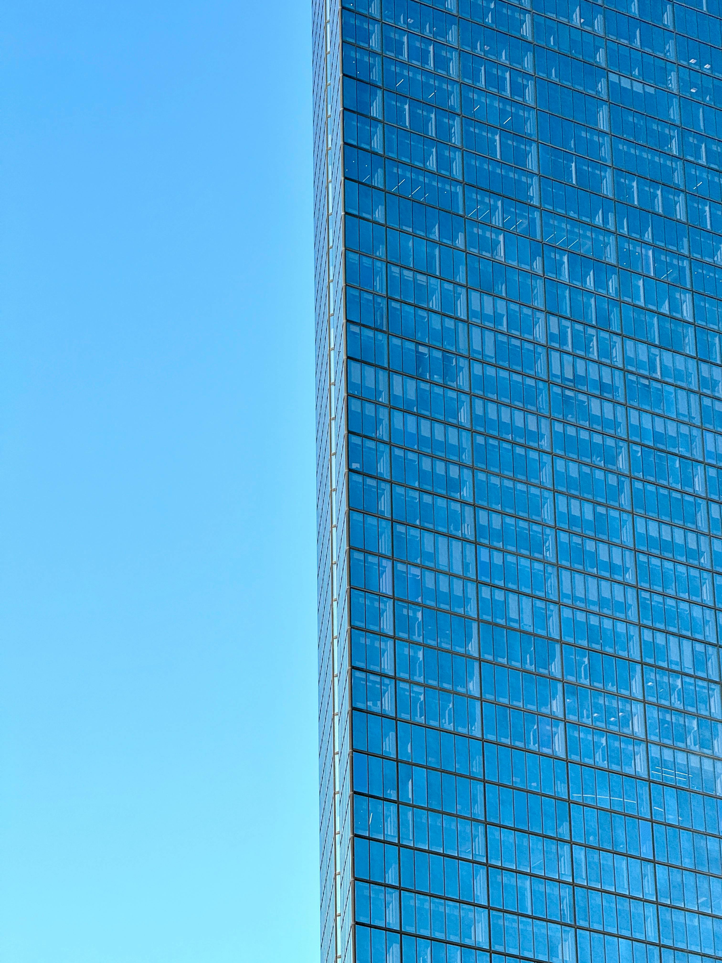бесплатная Возвышающийся стеклянный небоскреб с отражающими окнами под чистым голубым небом. Стоковое фото