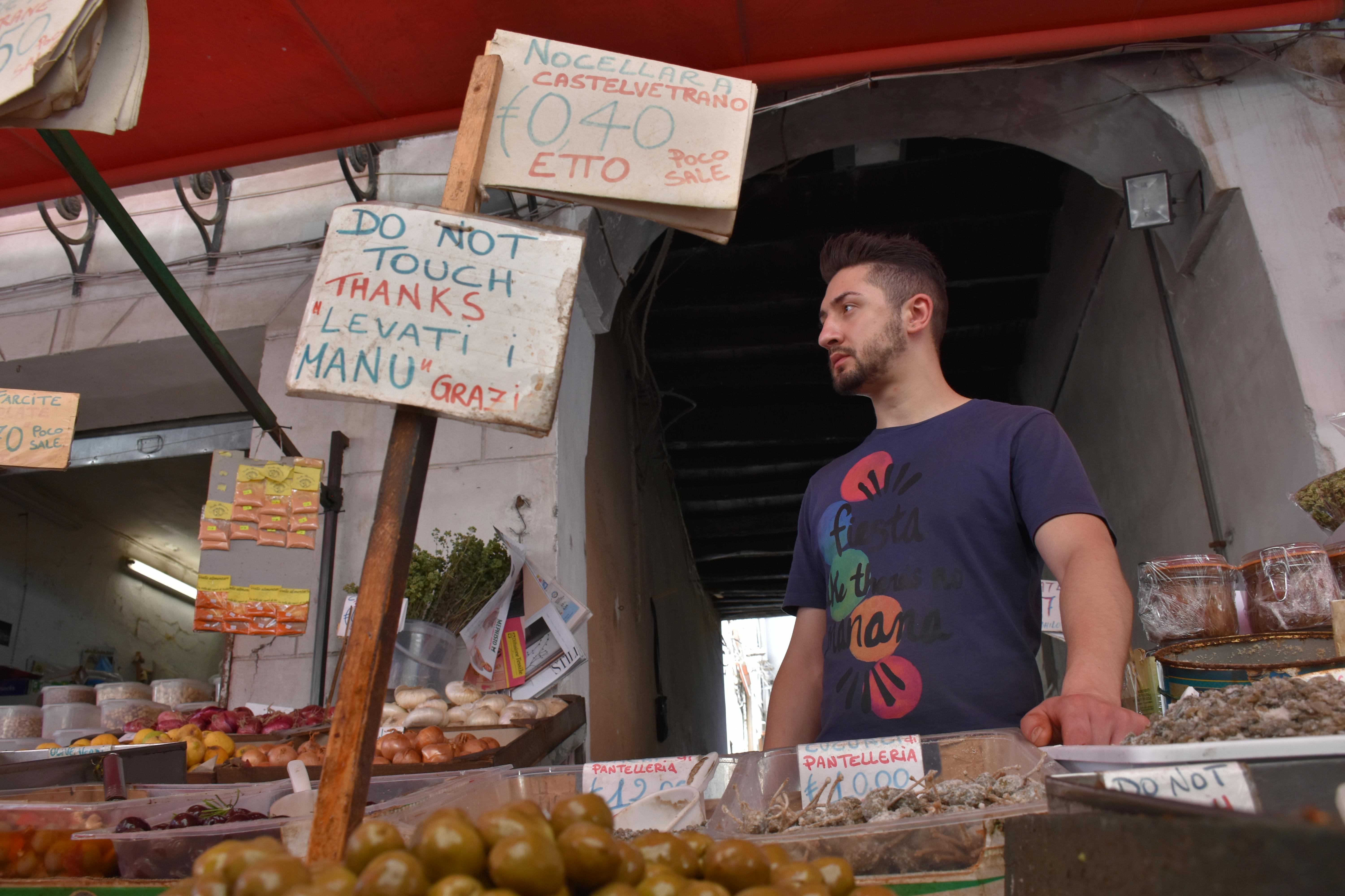 A man at a food stall in a bustling Palermo market.