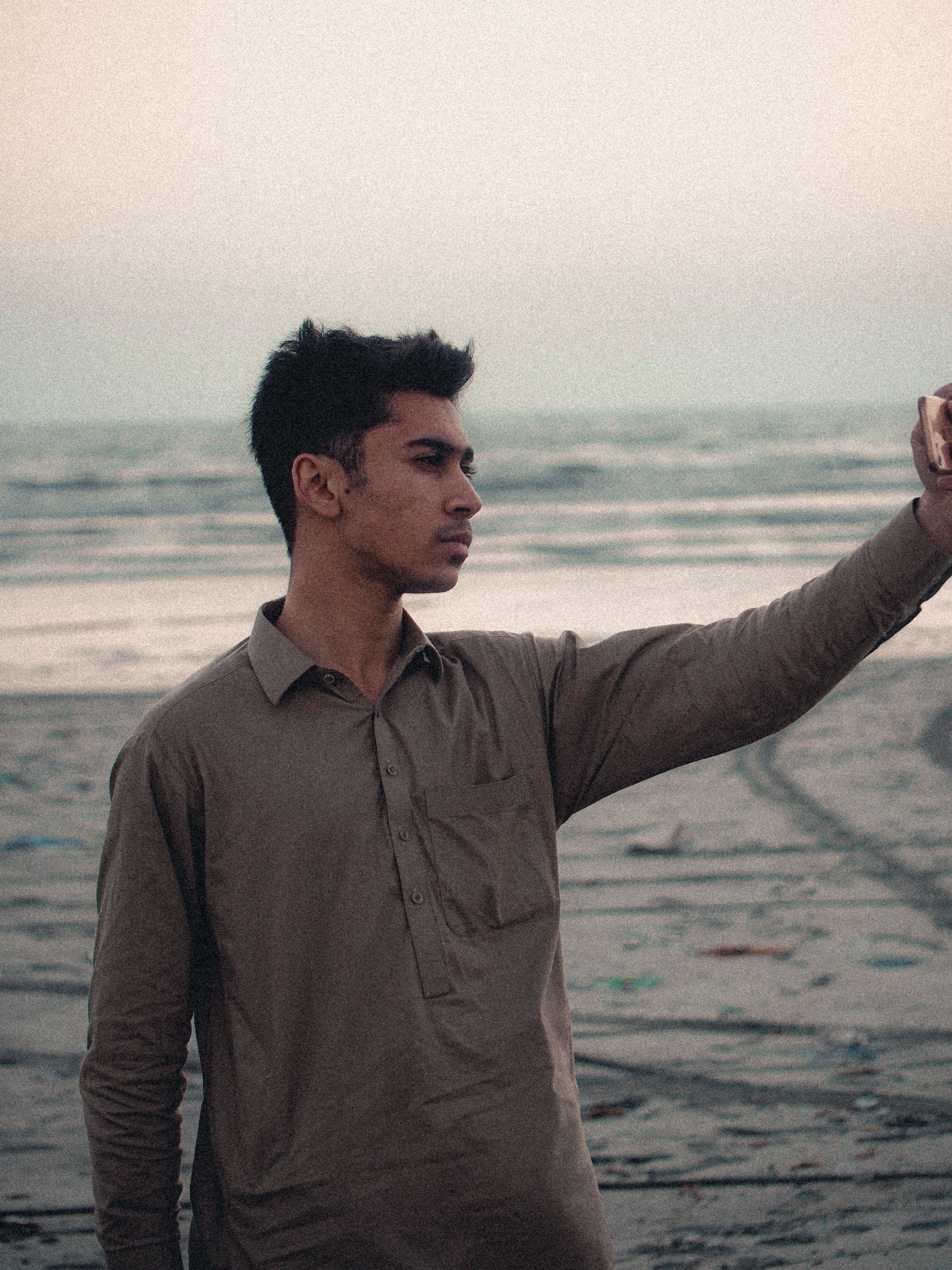 A young man takes a selfie at a serene beach during dusk, capturing the tranquil ocean background.