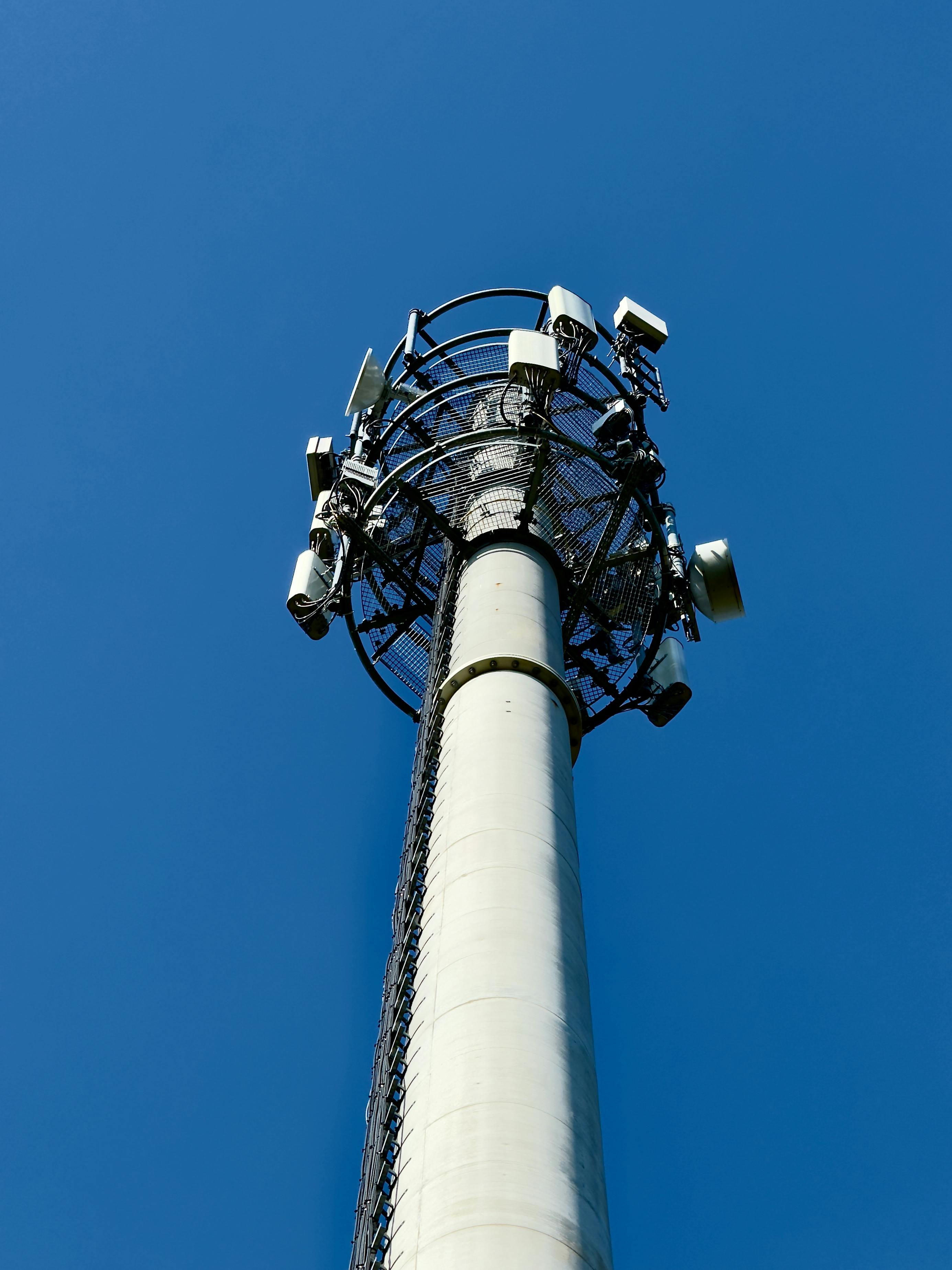 無料 明るい青空を背景に、通信技術を象徴する複数のアンテナを備えた高い携帯電話基地局。 写真素材