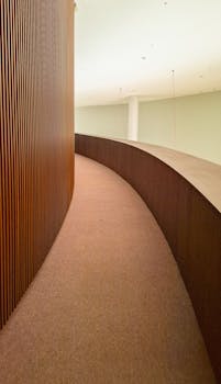 A sleek indoor walkway with a minimalist design, featuring a curved wooden wall.