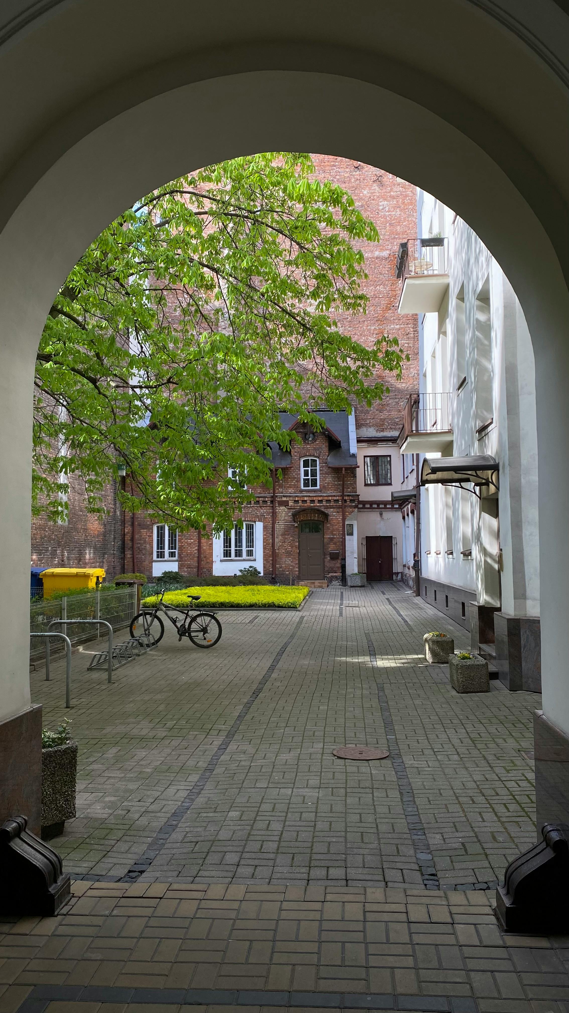 бесплатная Тихий внутренний дворик в Варшаве, Польша, с велосипедами и пышной зеленью под кирпичной аркой. Стоковое фото