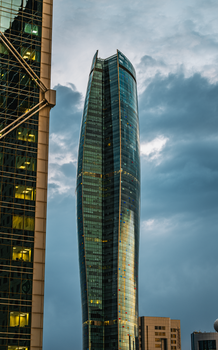 A striking modern skyscraper towers against a dramatic cloudy sky in Kuwait City, showcasing urban architecture.