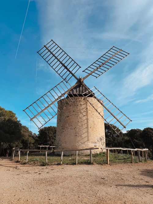 Free A charming vintage stone windmill set in a serene countryside landscape under a clear blue sky. Stock Photo