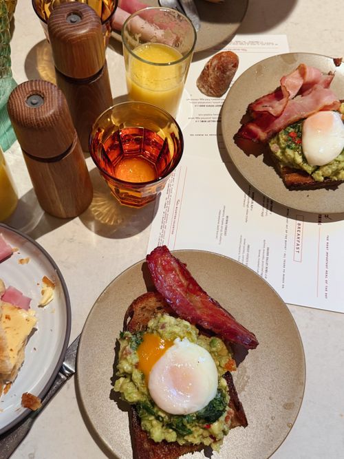 Free Gourmet breakfast featuring avocado toast, poached egg, bacon, and juice. Stock Photo