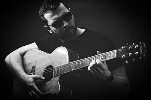 Gray scale of Man in Black Sunglasses Playing Acoustic Guitar