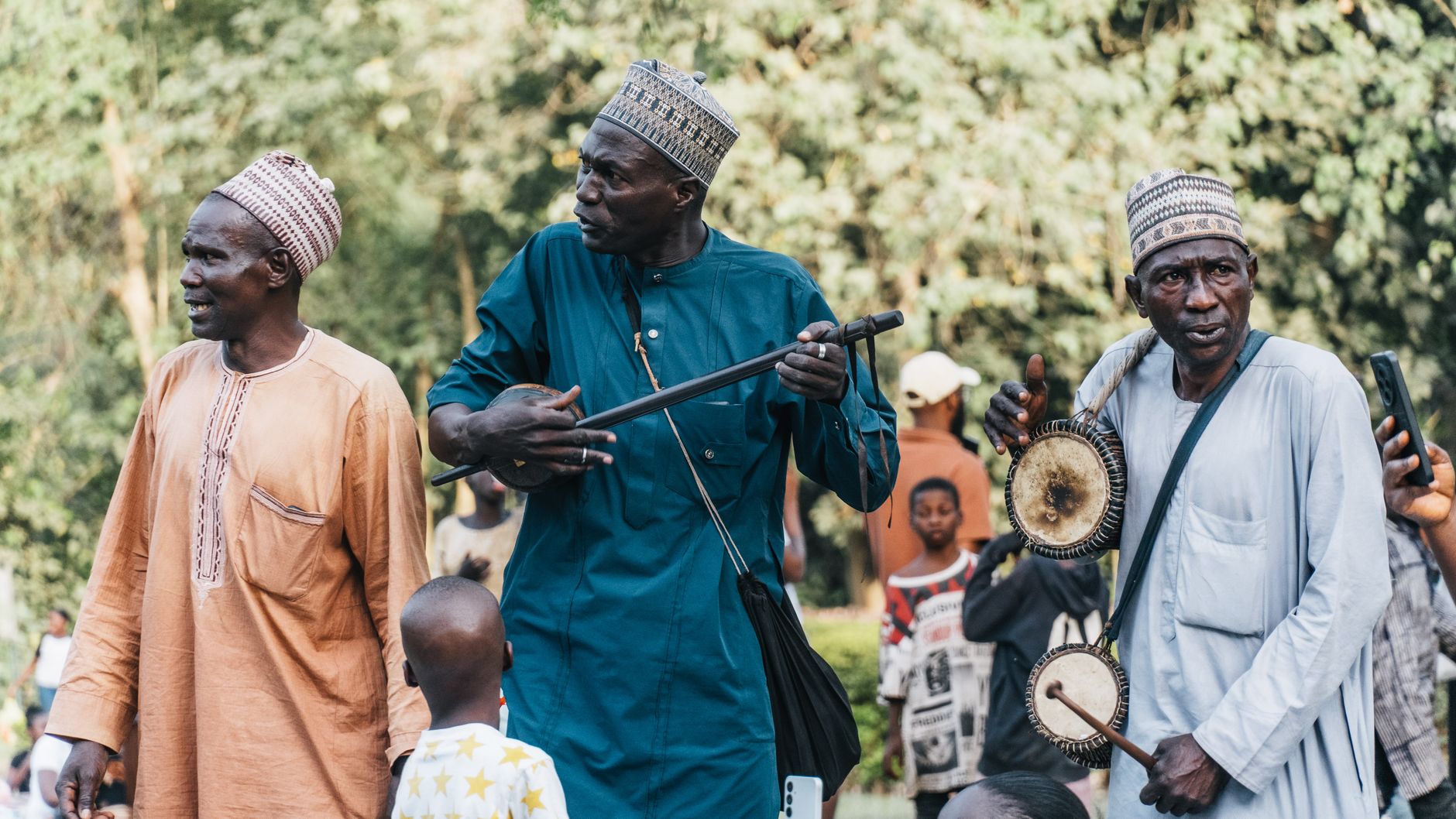 Three African musicians perform with traditional instruments outdoors.