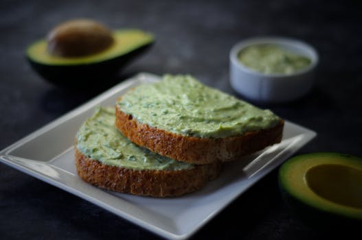 Delicious avocado spread on toast with fresh avocado halves and a dipping sauce.