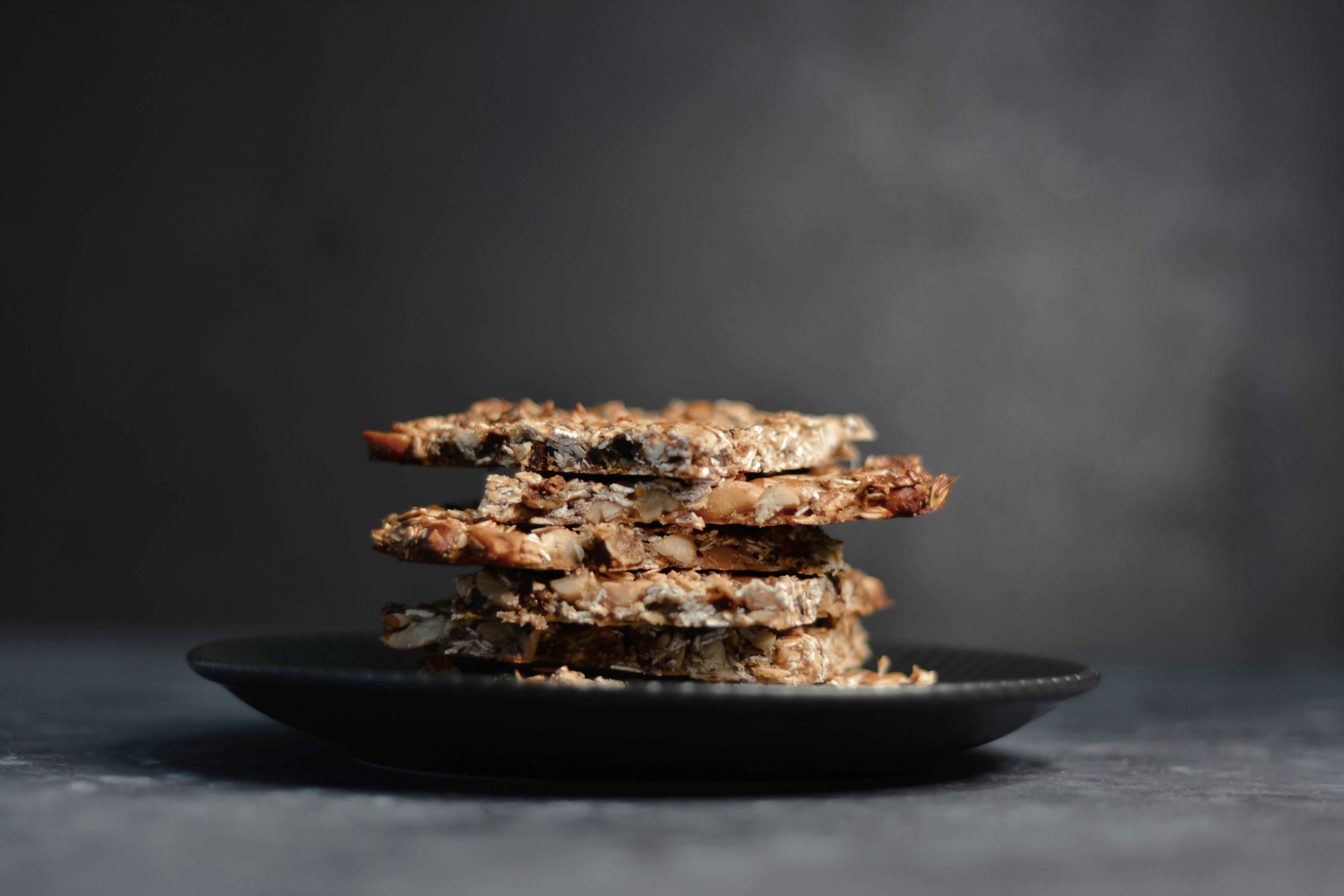Close-up of a stack of homemade granola bars on a dark plate against a moody background.