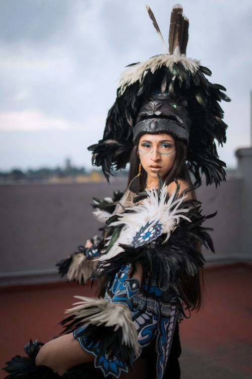 Free Woman in elaborate Aztec-inspired costume with feathered headdress on a rooftop. Stock Photo