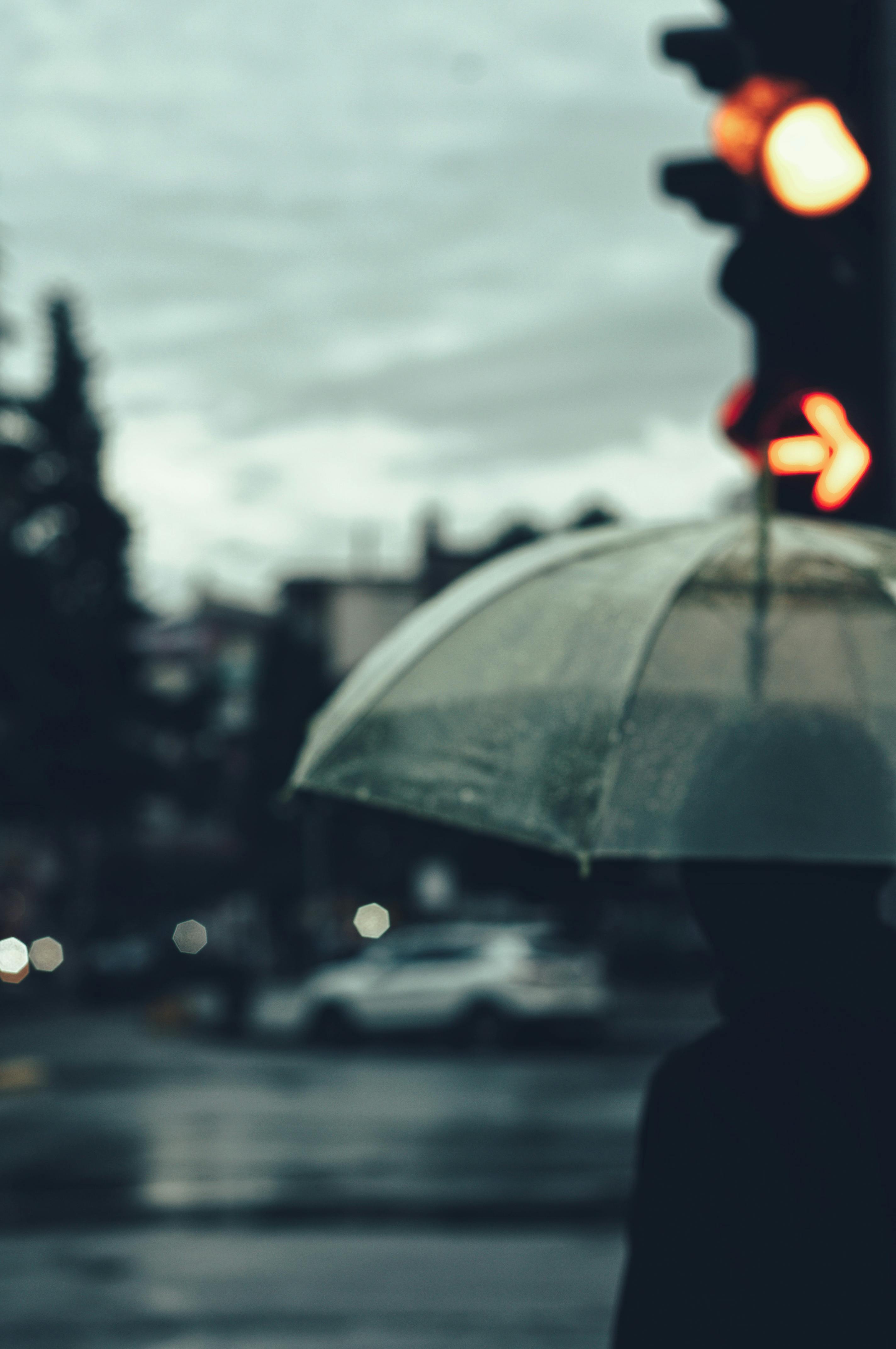 Free Silhouette of person with umbrella under streetlight on rainy night, capturing moody urban ambiance. Stock Photo