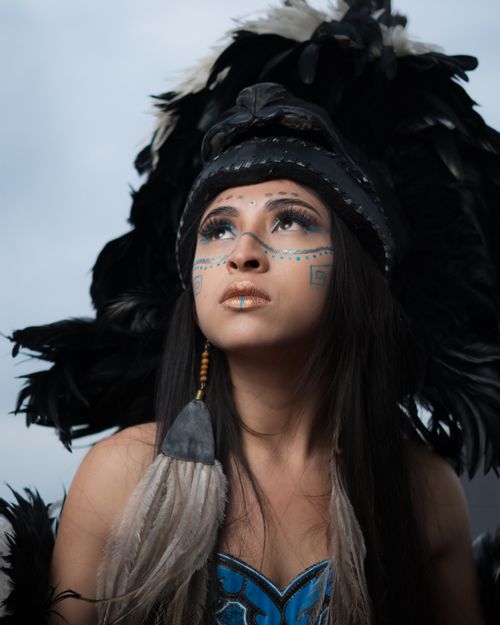 Free A woman with face paint and feathered headdress gazes upwards in a traditional attire. Stock Photo