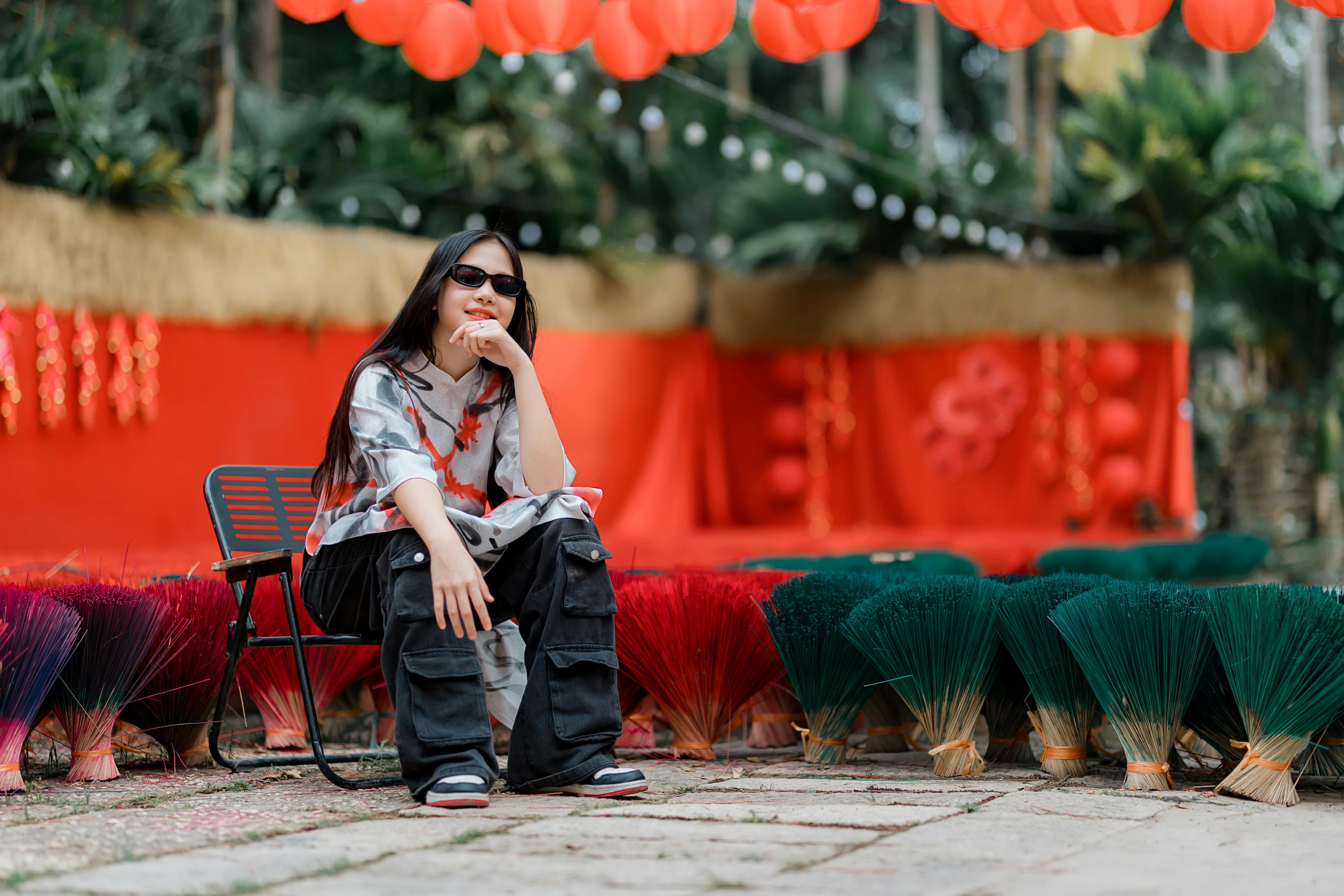 бесплатная Женщина в повседневной одежде сидит в окружении связок разноцветных благовонных палочек под праздничными красными украшениями. Стоковое фото