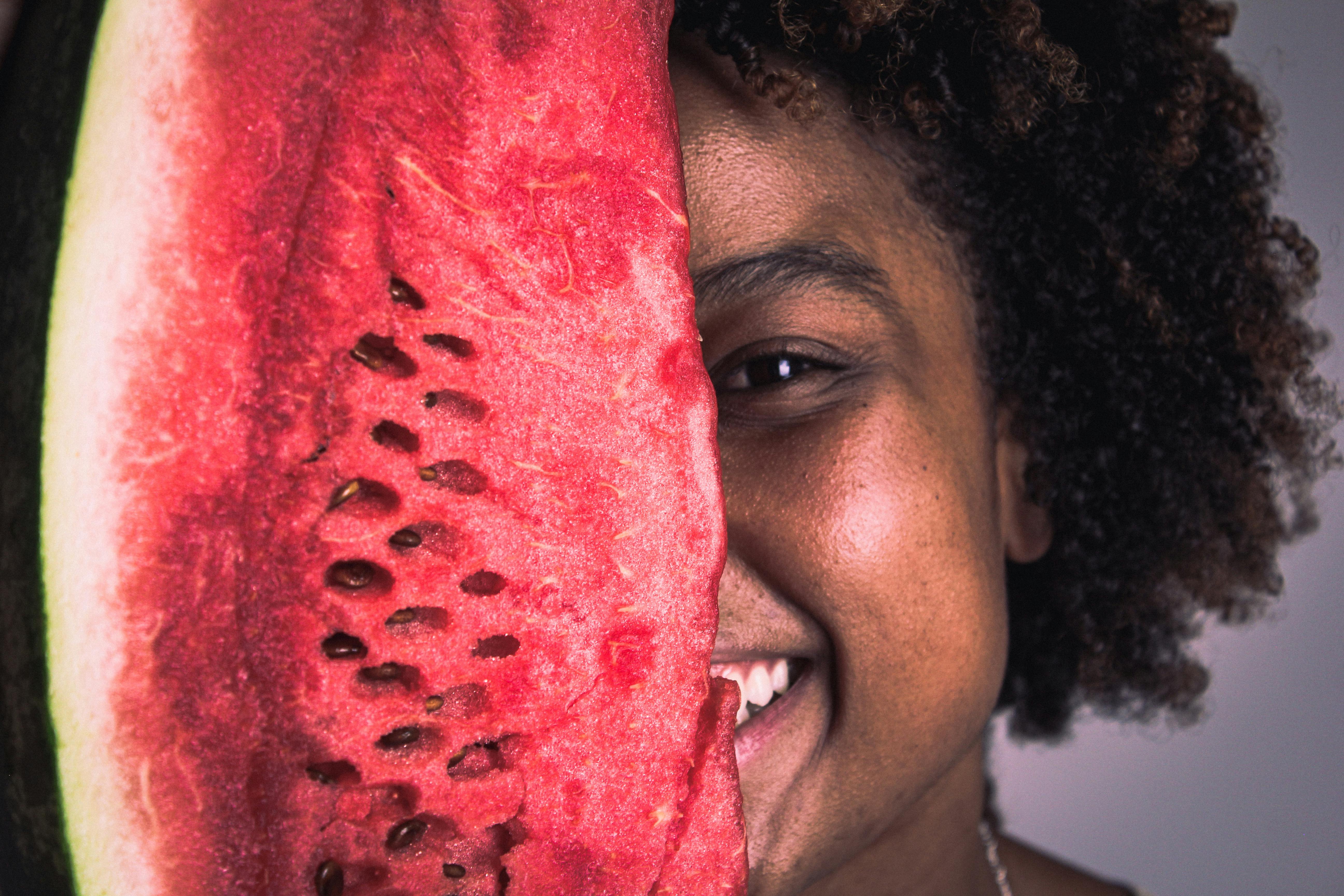 Free A joyful woman holding a watermelon slice covering half of her face, showcasing happiness and freshness. Stock Photo