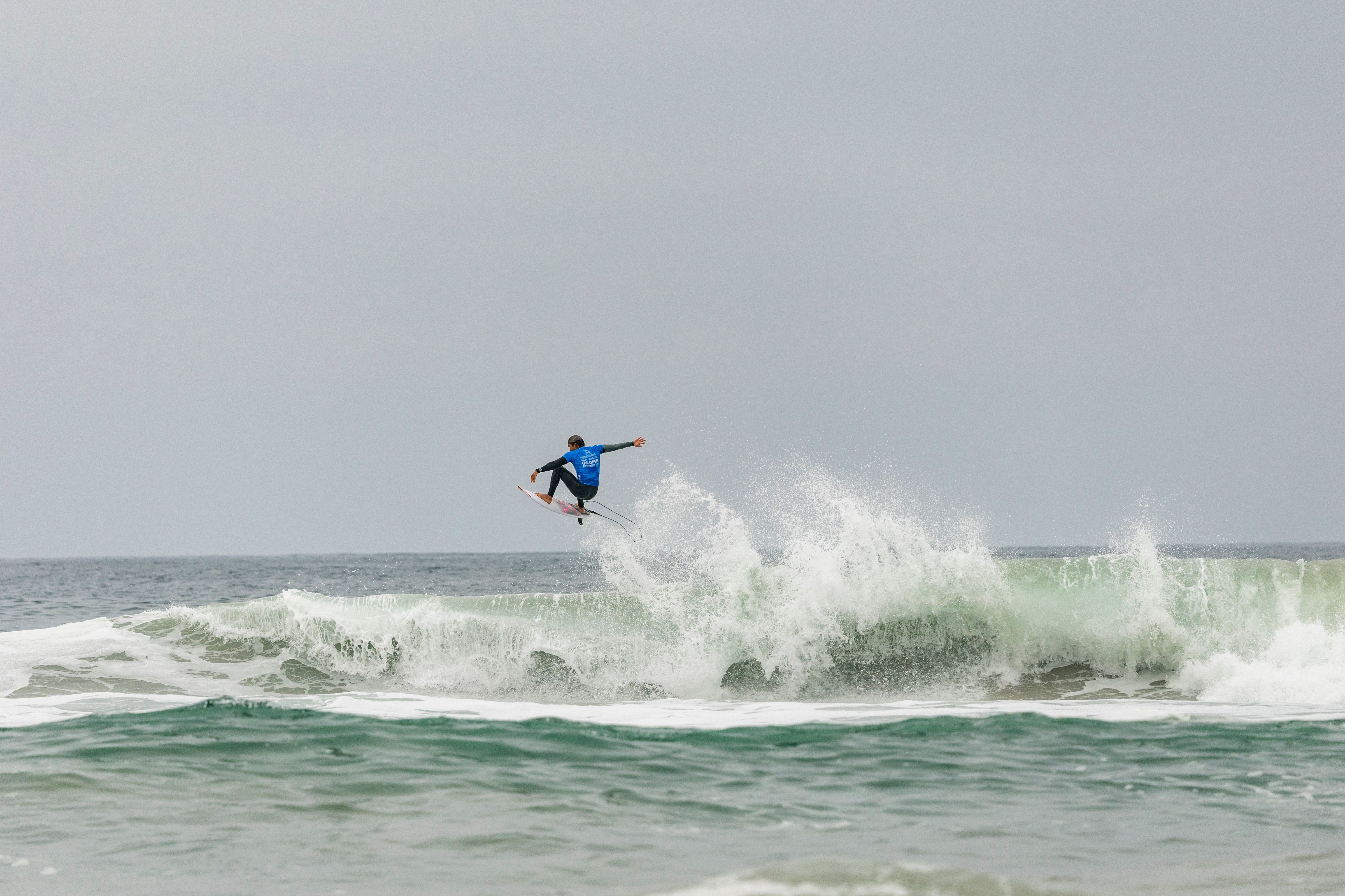 Surfer performing aerial trick on large ocean waves, showcasing skill and excitement.