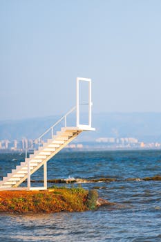 A white staircase leads to an open door against a seaside backdrop, evoking surreal and imaginative themes.