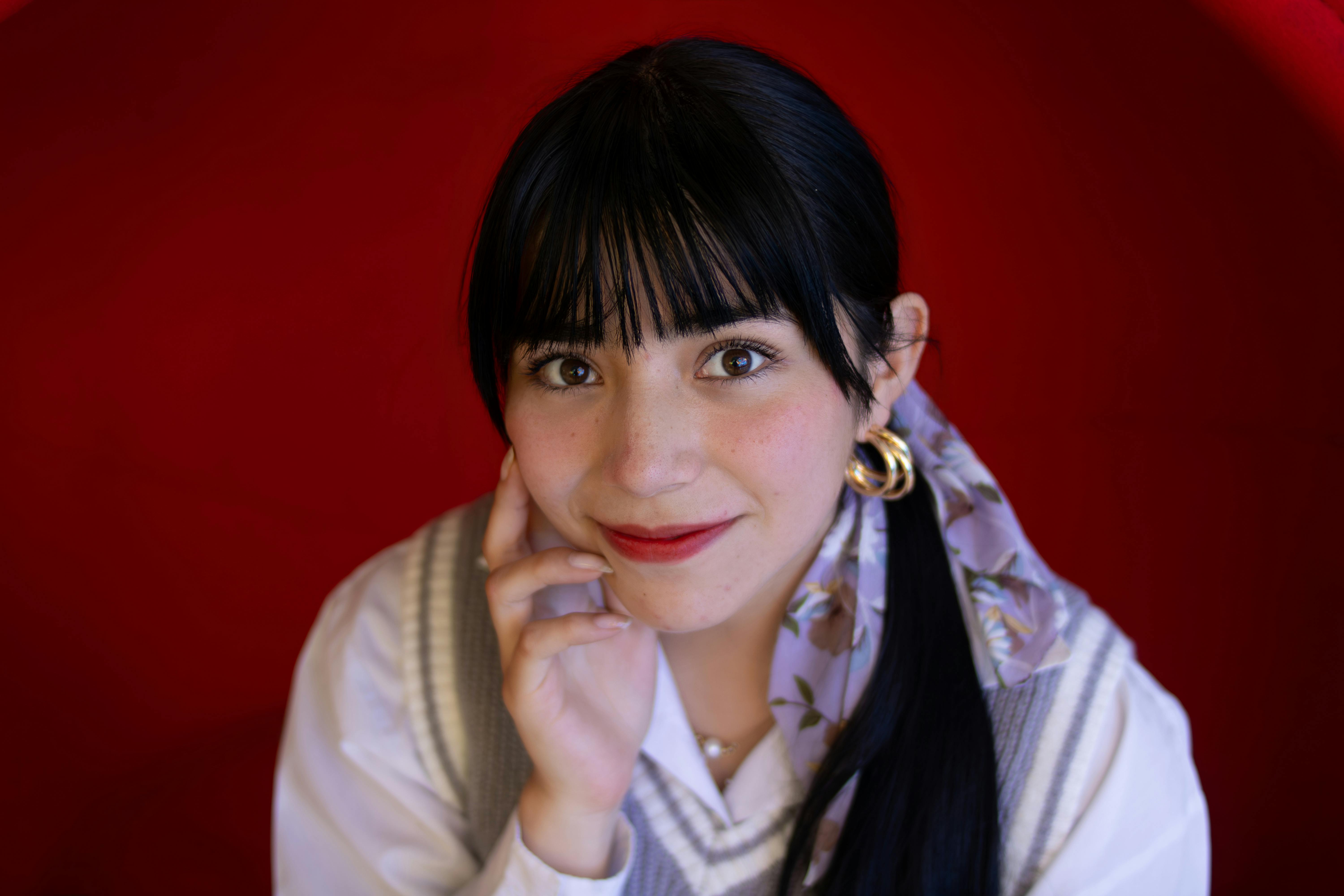 Gratis Smilende kvinde iført tørklæde og øreringe med en rød baggrund. Lagerfoto