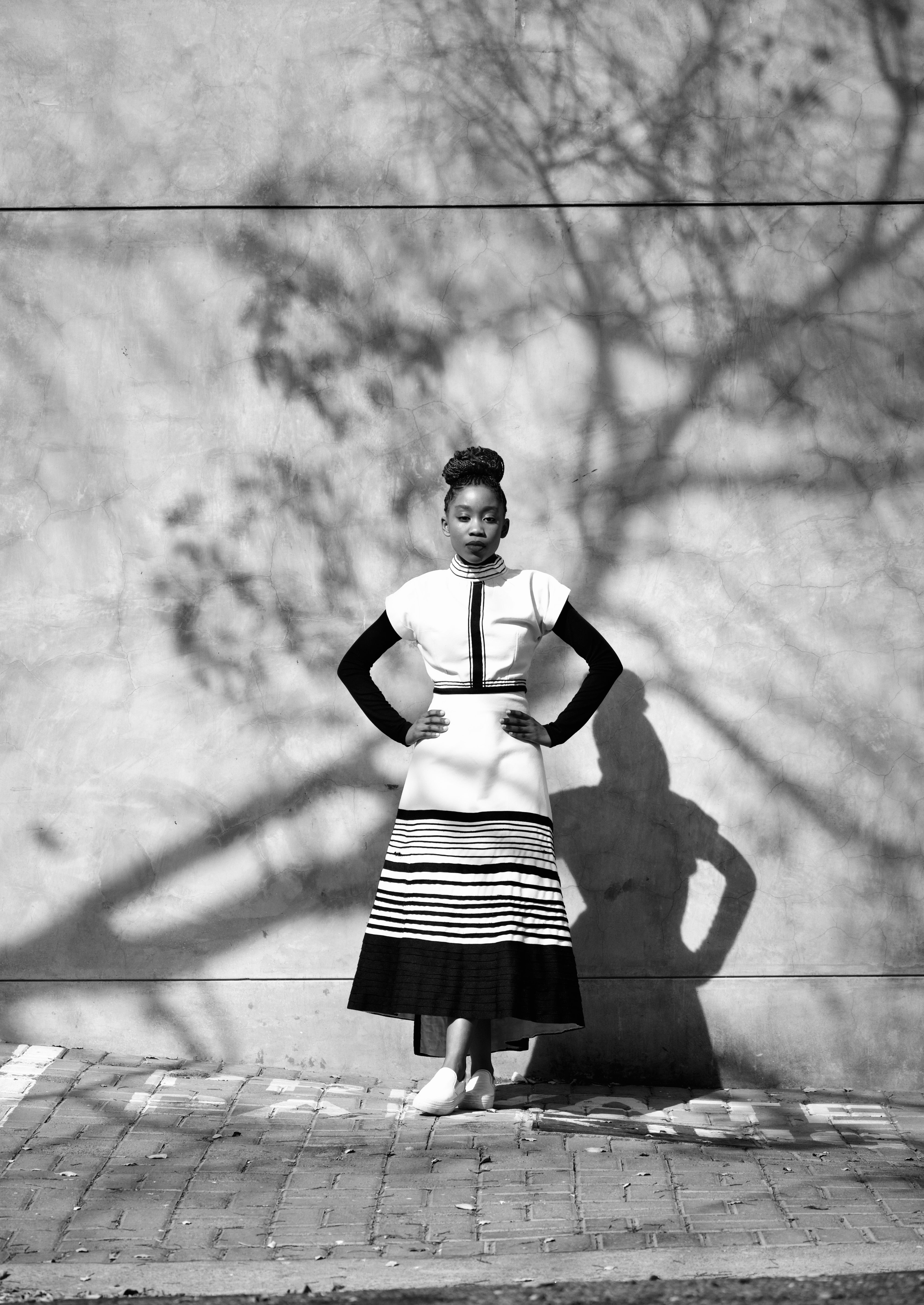 Elegant woman poses against wall with tree shadows, showcasing fashion style.
