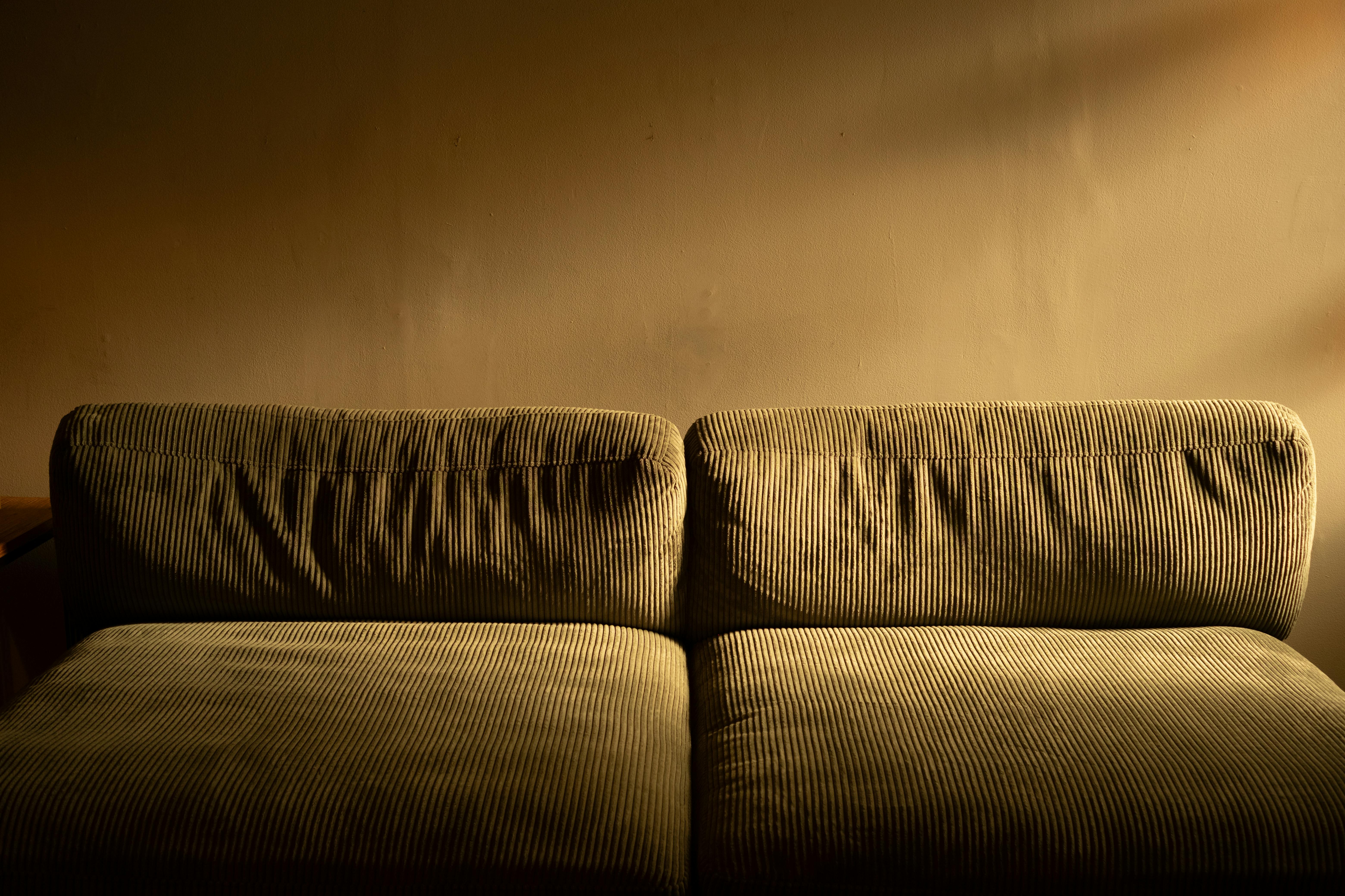 Kostenlos Ein weiches Cordsofa, das in warmes Umgebungslicht getaucht ist – perfekt für gemütliche Interieurs. Stock-Foto