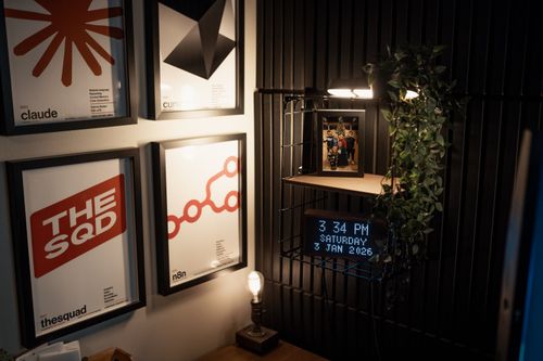 Free Stylish home office featuring retro posters, a digital clock, and ambient lighting for a cozy workspace. Stock Photo