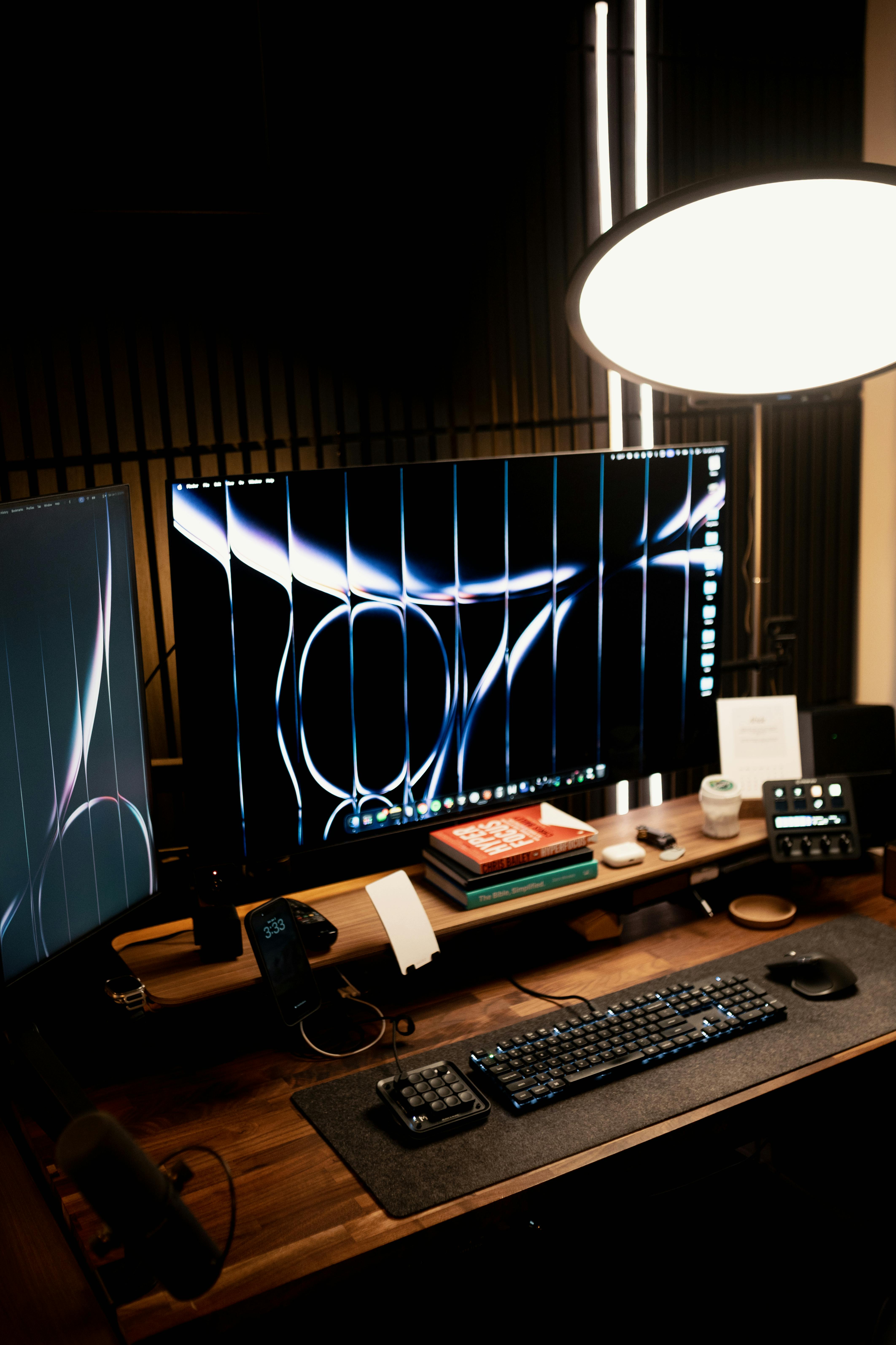 бесплатная Стильный домашний офисный стол с двумя мониторами, аксессуарами и теплым освещением для повышения продуктивности. Стоковое фото