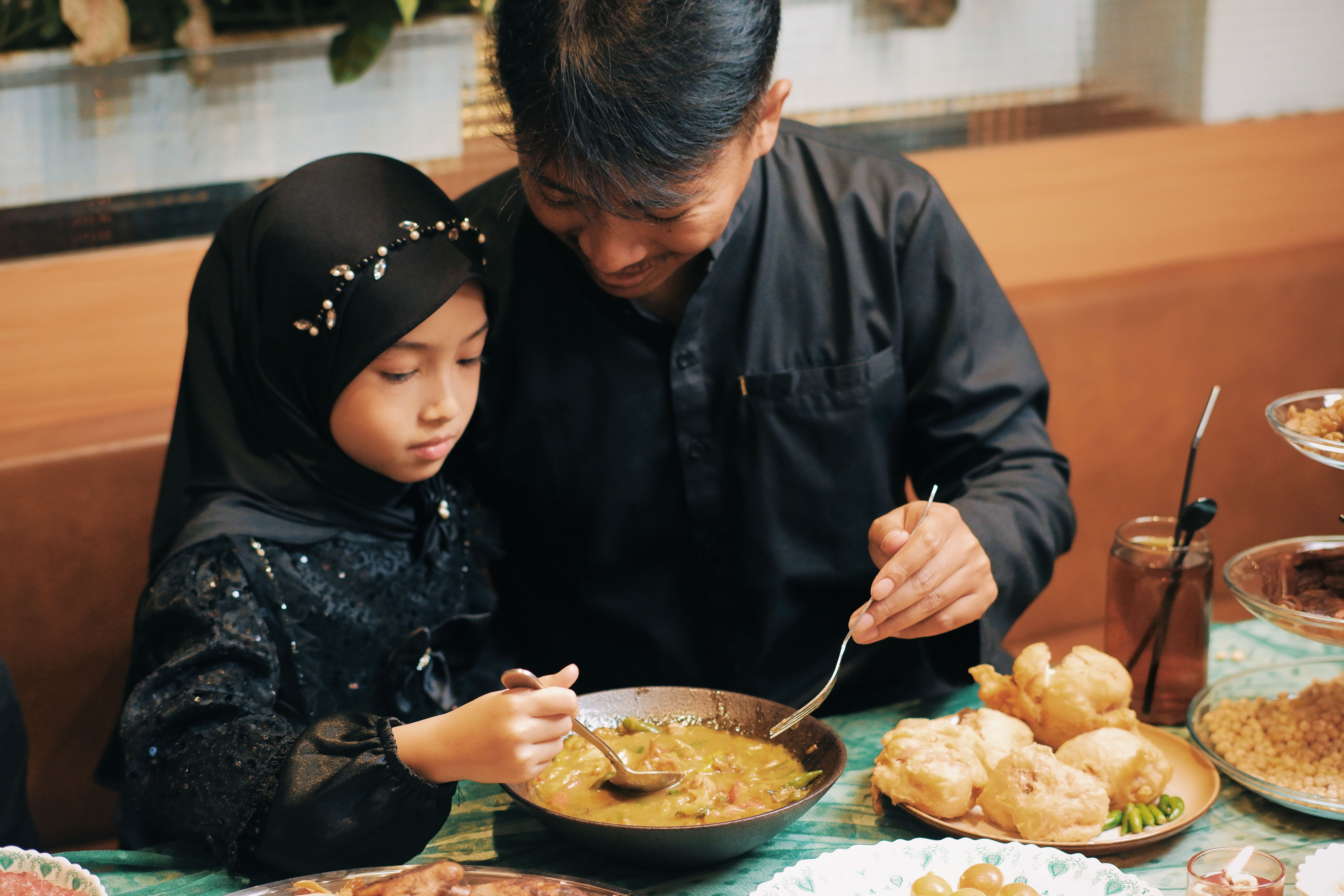 Ayah dan anak perempuan berbagi makanan tradisional, mengabadikan momen keluarga yang hangat di Indonesia.