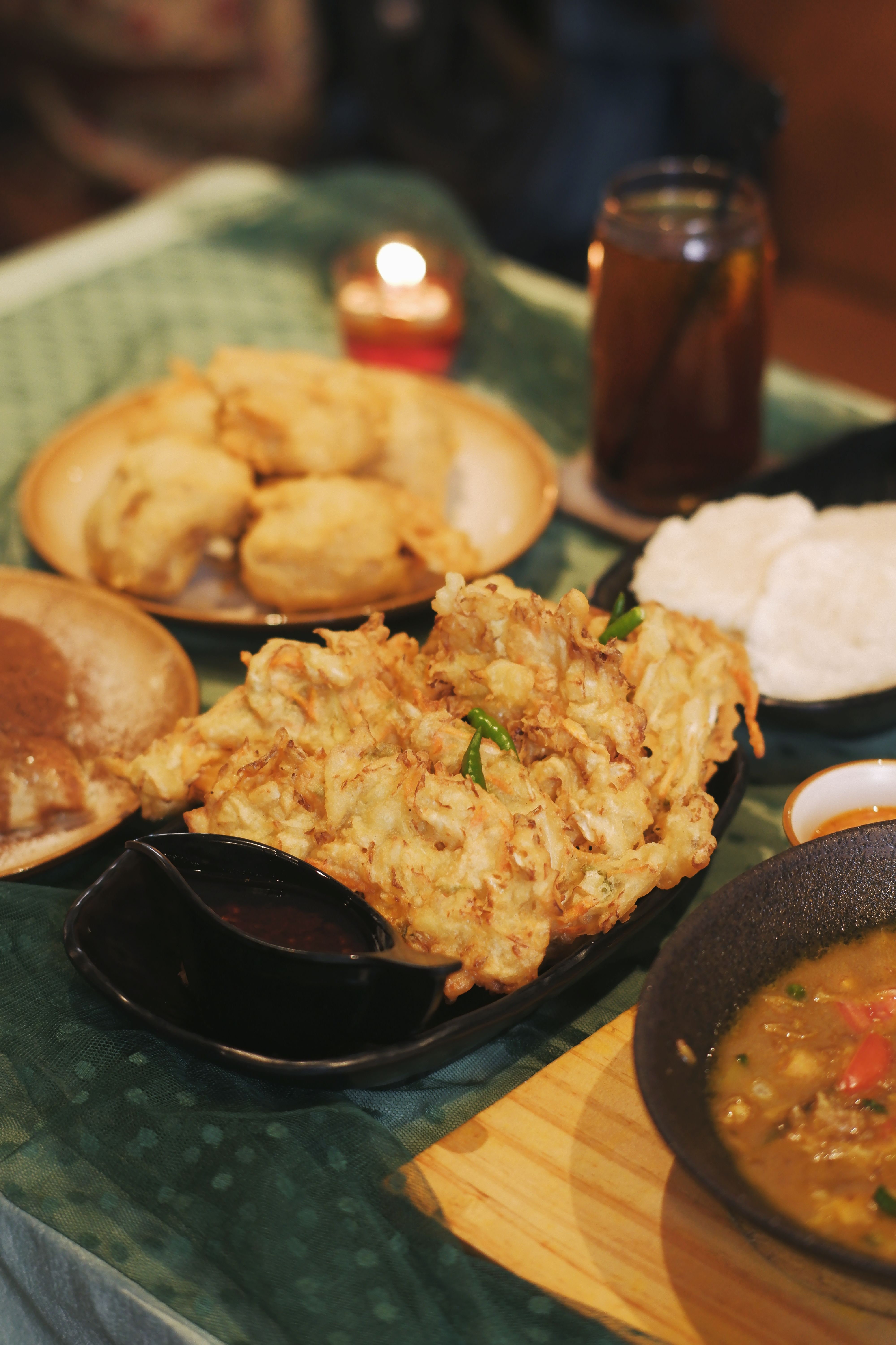 Traditional Indonesian meal featuring gorengan, sambal, and tea served on a green tablecloth.