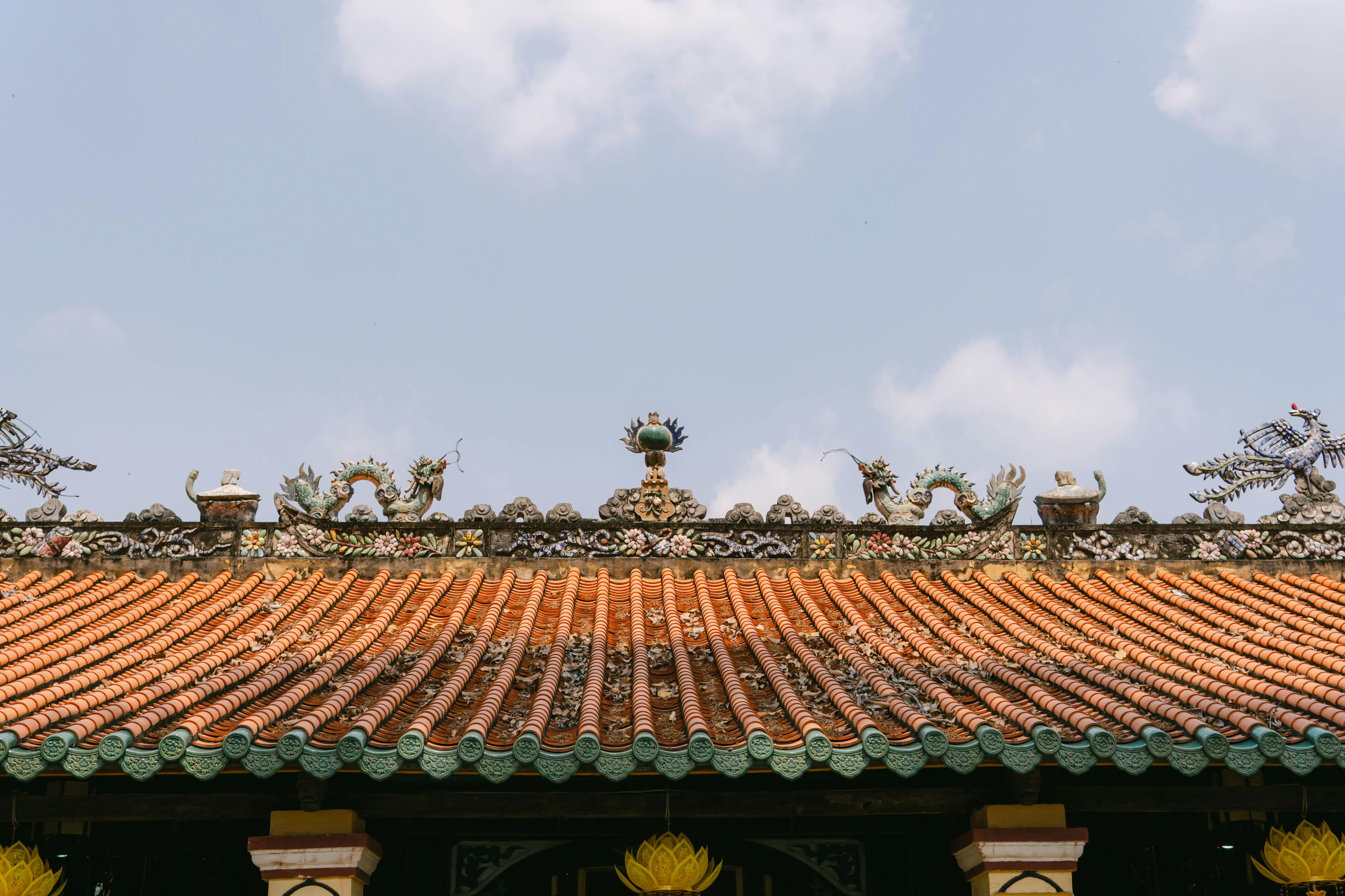 Gratis En detaljert visning av et tradisjonelt tempeltak utsmykket med utsmykkede drageskulpturer under en klar blå himmel. Arkivbilde