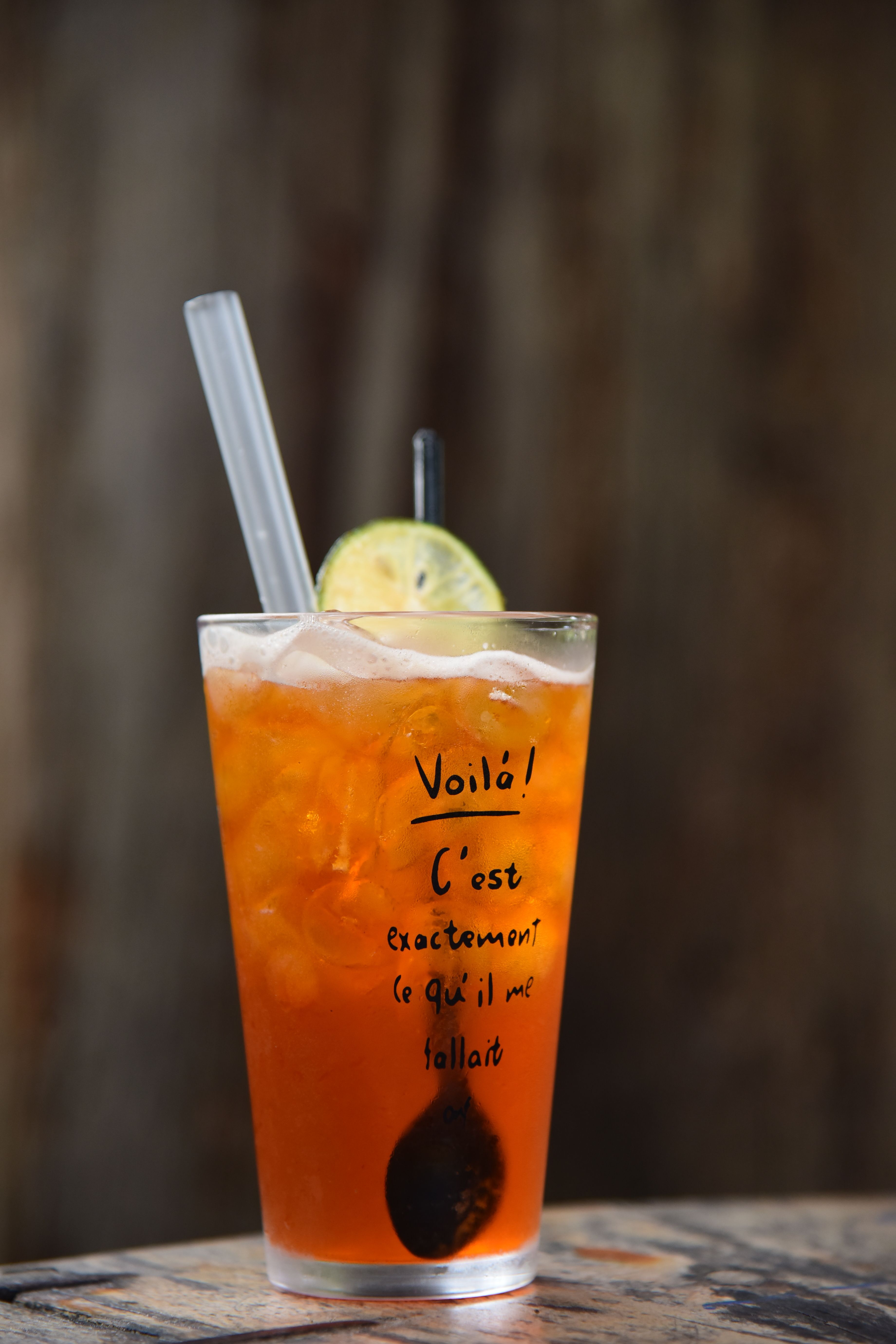 Tall glass of citrus iced tea with ice cubes, lime slice, and straws against a rustic background.