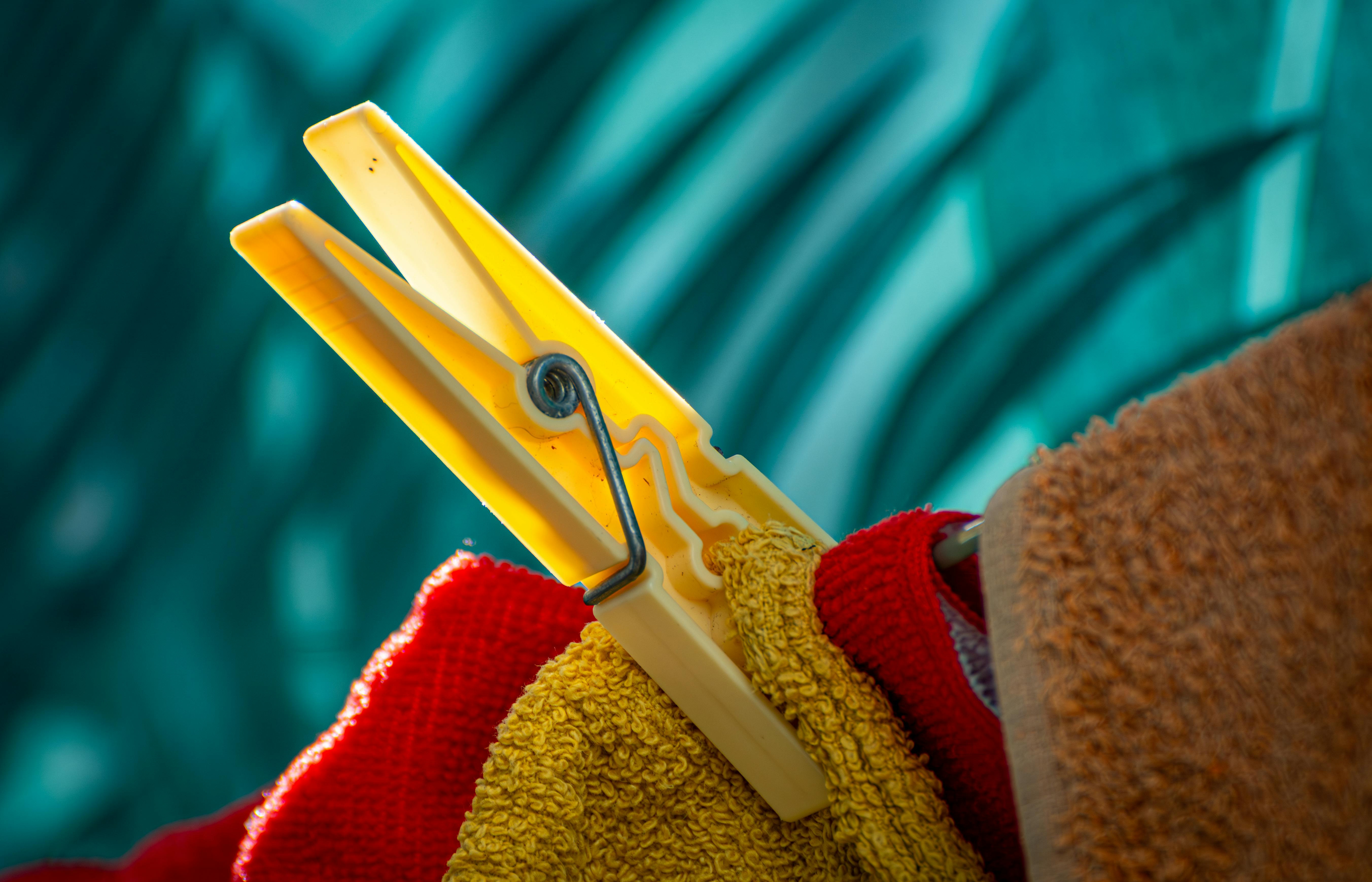 Gratuit Une pince à linge jaune vif accroche des serviettes colorées sur un fond bleu flou, créant un contraste saisissant. Photos