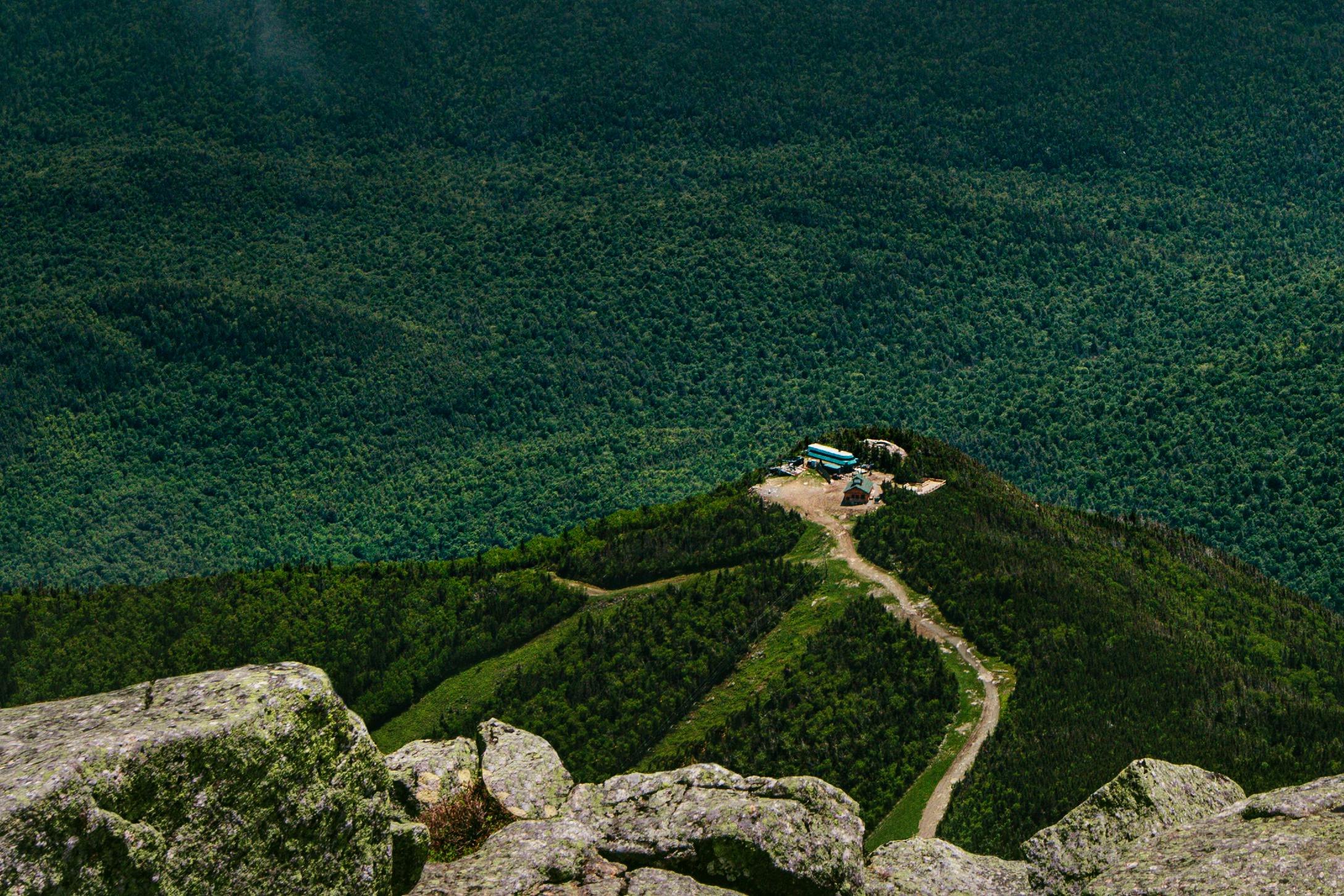 A scenic aerial shot of a lonely cabin atop a mountain surrounded by dense forest, showing natural beauty.