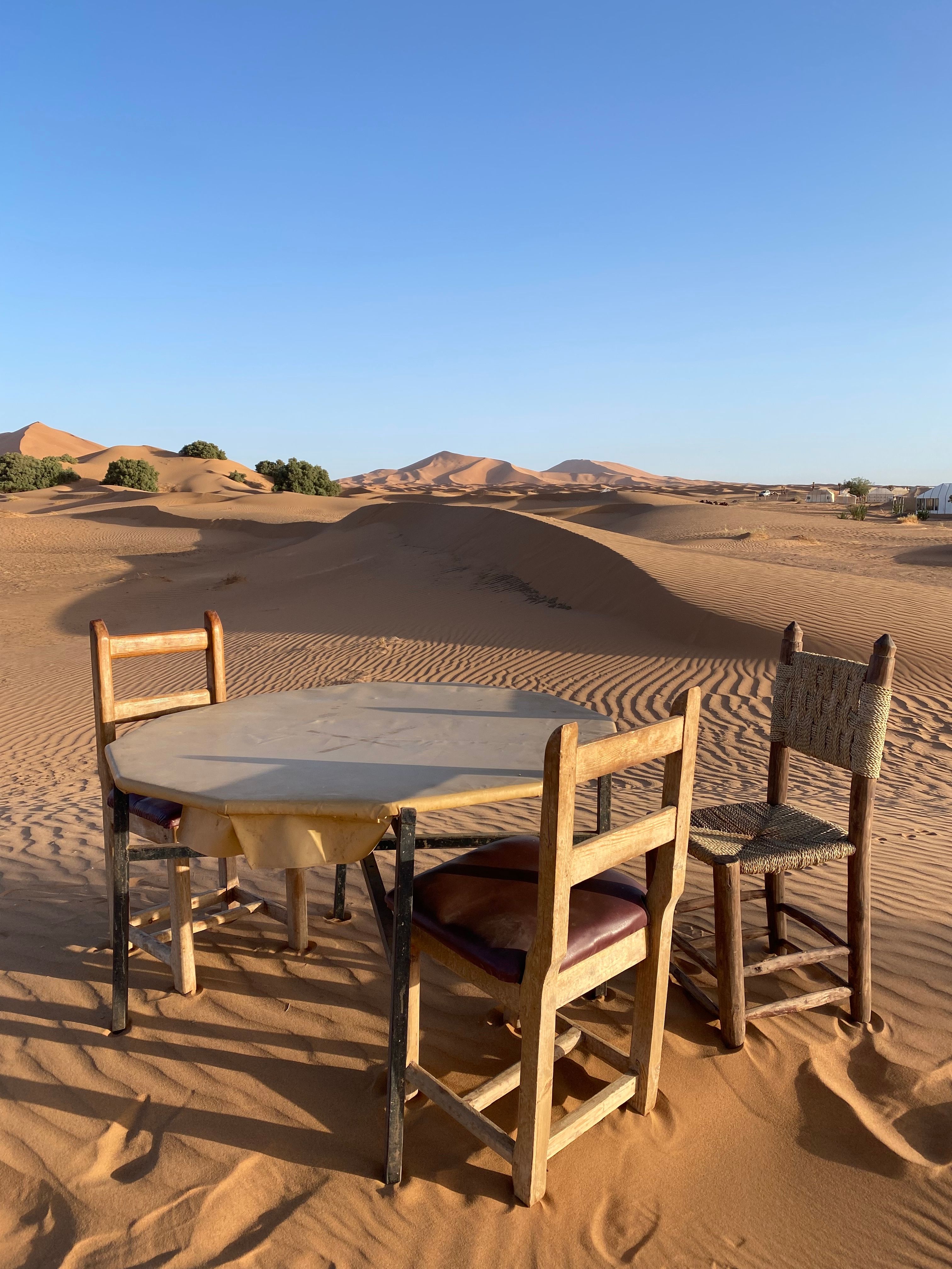 Vintage wooden chairs and table in the golden sand dunes of Erg Chebbi, Morocco.