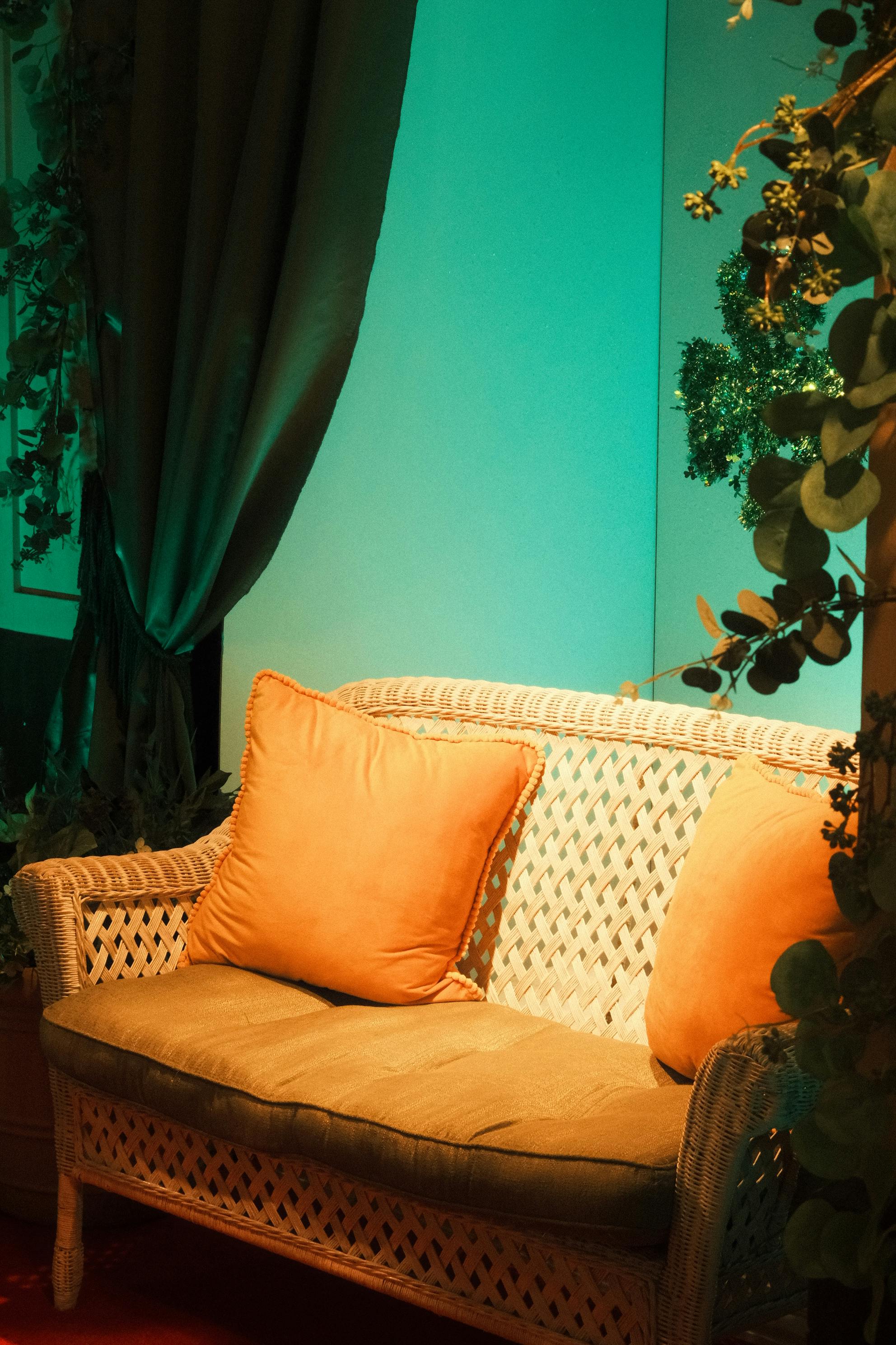 無料 温かみのある照明が当たる室内に、オレンジ色のクッションが付いた快適な籐ソファが置かれています。 写真素材