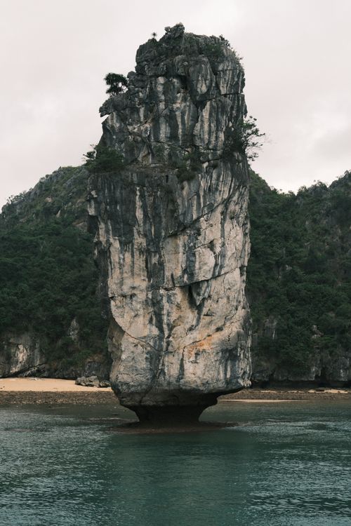 Free A towering limestone karst rises dramatically from the sea, surrounded by tranquil green waters and lush cliffs. Stock Photo