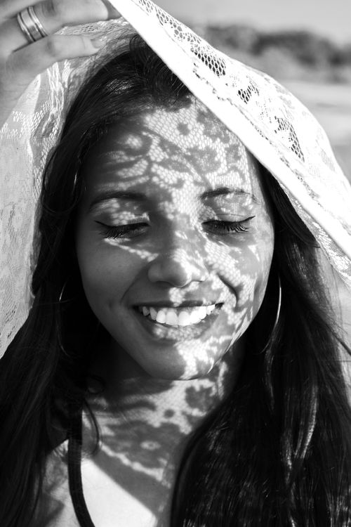 Free A striking black and white portrait of a smiling woman with lace shadows on her face. Stock Photo