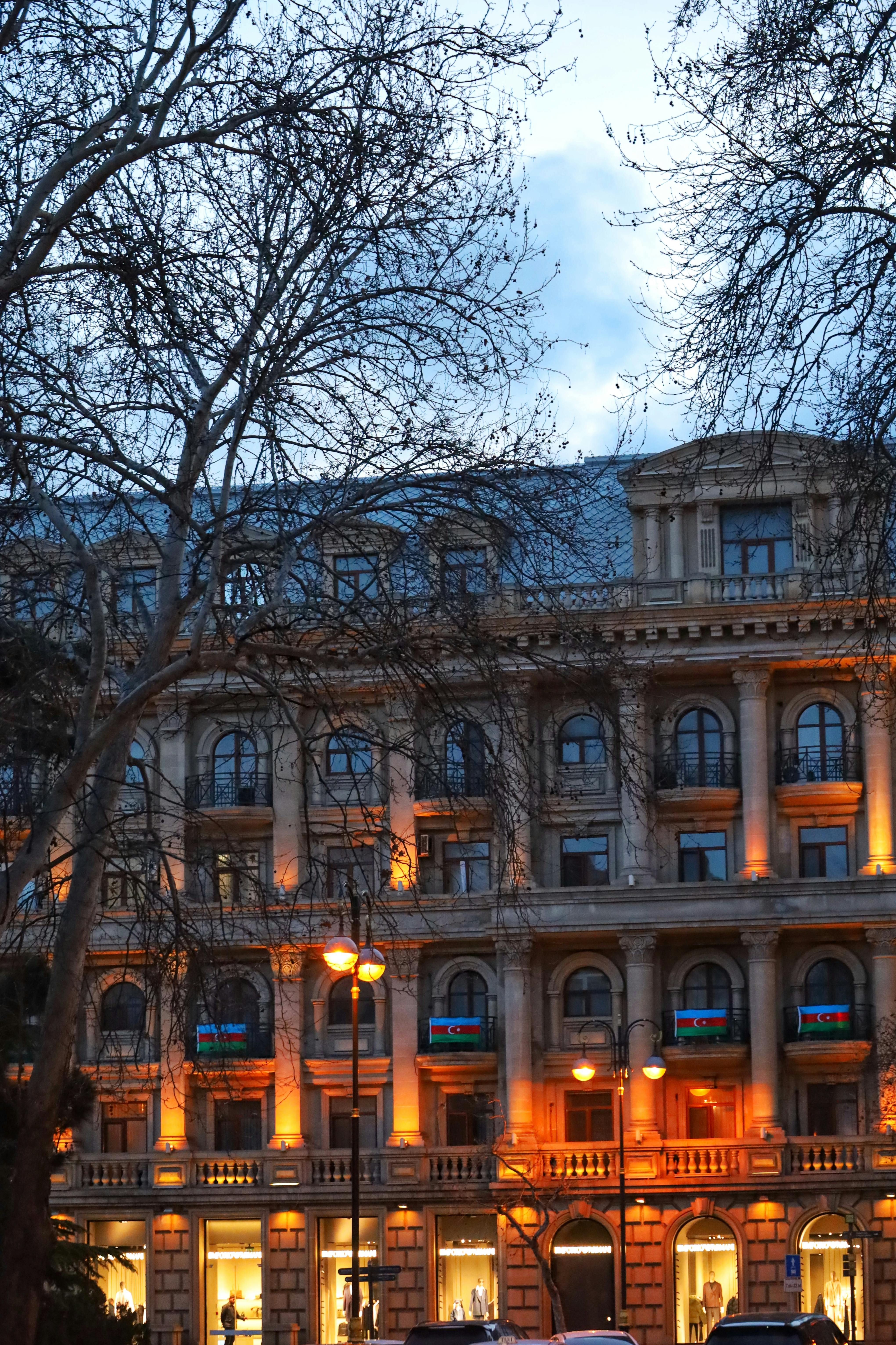 無料 夕方の照明と葉のない木々が空と対照をなす、美しく照らされた歴史的建造物。 写真素材