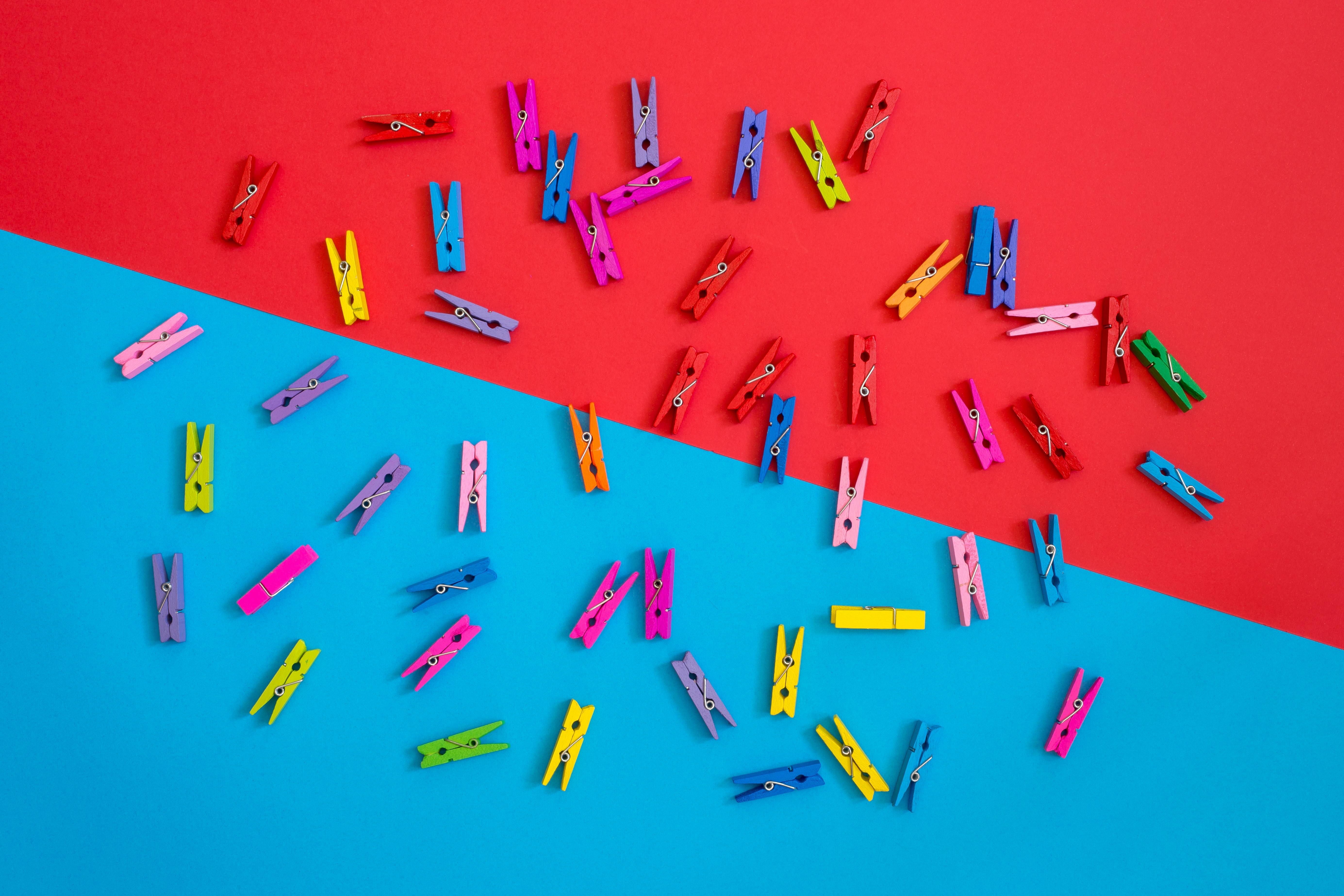 Colorful clothespins scattered on a contrasting red and blue background for a vibrant look.