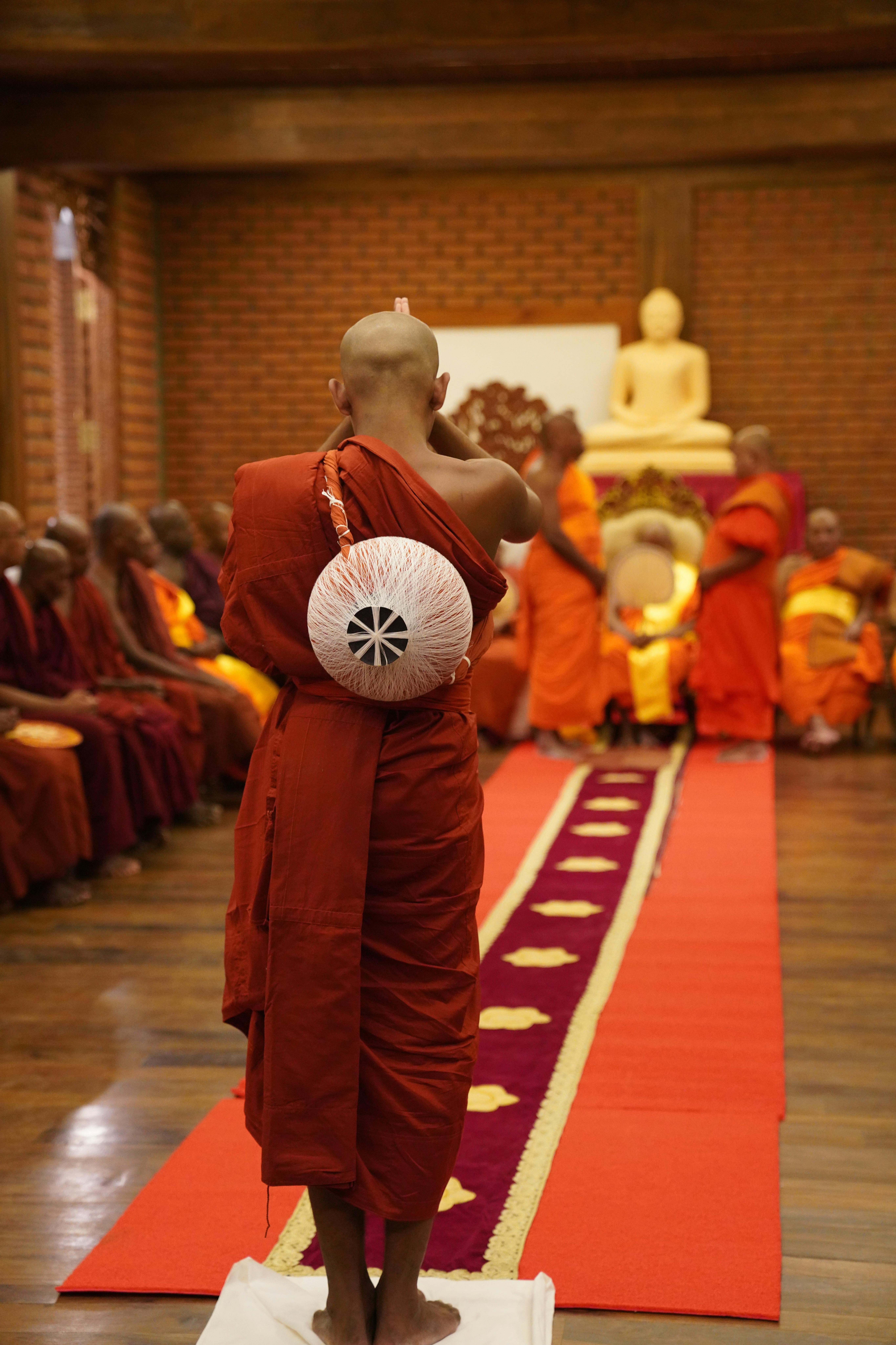 無料 伝統的な僧衣をまとった仏教僧が、屋内で仏像とともに儀式に参加している。 写真素材