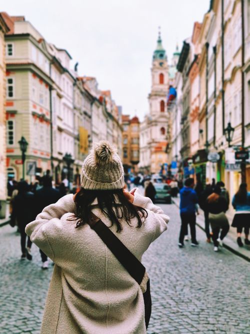 Free A tourist photographs a vibrant street view in Prague, showcasing historic architecture and lively atmosphere. Stock Photo