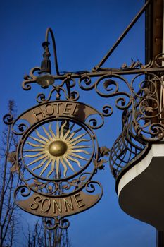 Artistic metal Hotel Sonne sign with sun emblem against clear blue sky.