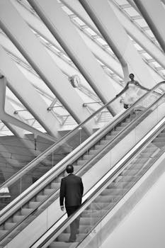 Black and white image of people on escalators in a modern architectural space.